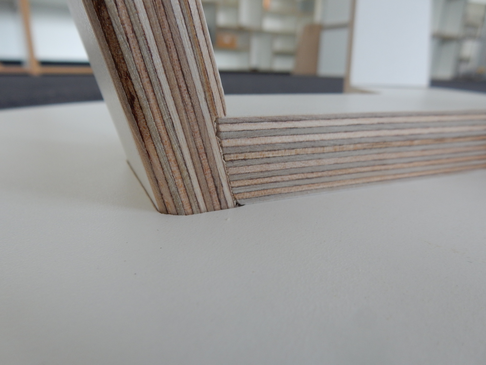 Detailaufnahme vom Tojo Rund Tisch 500: Tischbein aus Schichtholz trifft auf die weiße Tischplatte.