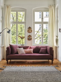 Burgunderrotes Sofa mit mehreren Vitra Kissen in verschiedenen Farben im hellen Wohnzimmer.