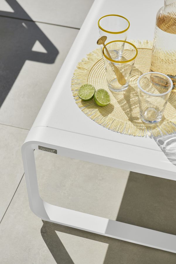 Detailaufnahme des weißen Fermob Bellevie Outdoor-Tisches mit Getränken und Limetten. Moderner, niedriger Gartentisch.