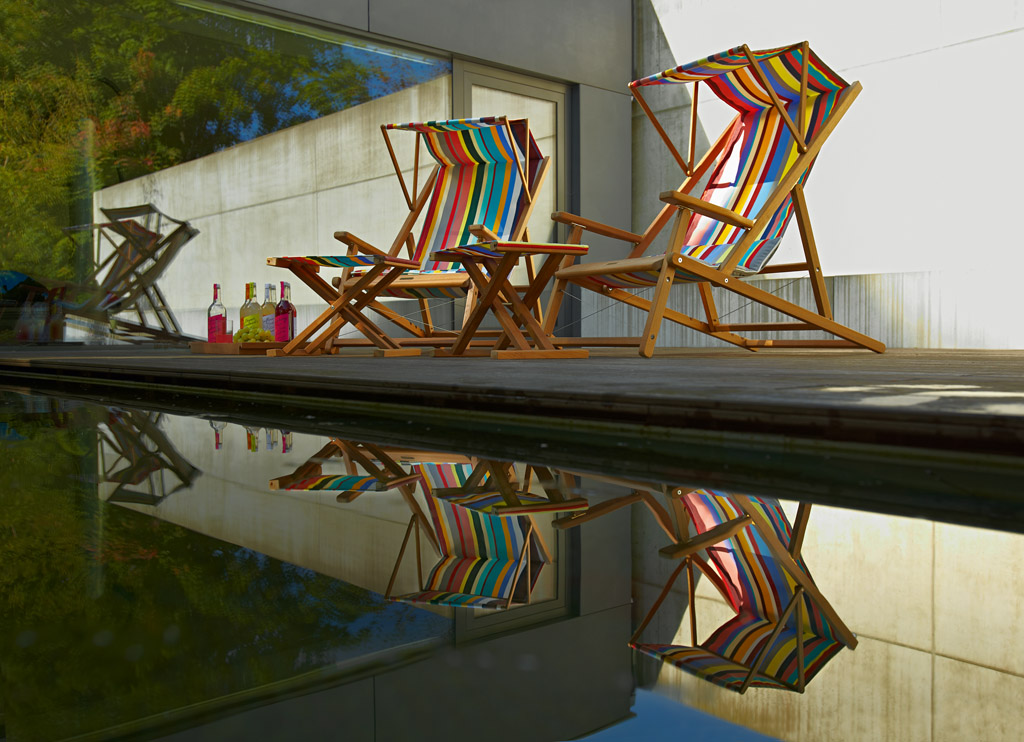 Zwei gestreifte Weishäupl Cabin Strandstühle aus Holz stehen im Freien am Pool.
