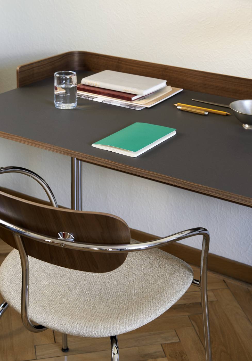 AndTradition Pavilion AV4 Armchair: Armlehnstuhl mit hellem Sitzpolster und Chromgestell am Schreibtisch.