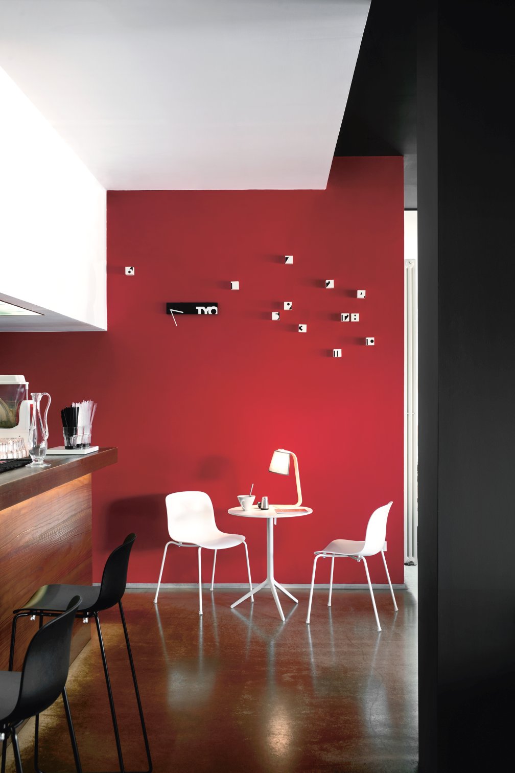 Heller Raum mit Magis Troy Chair Stühlen, Tisch und Lampe vor roter Wand, modernes Möbeldesign.