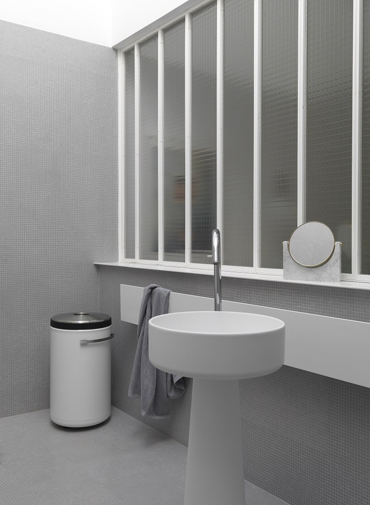 Weißer Vipp Wäschekorb im modernen Badezimmer mit Waschbecken, Spiegel und Fenster für stilvolle Badgestaltung.