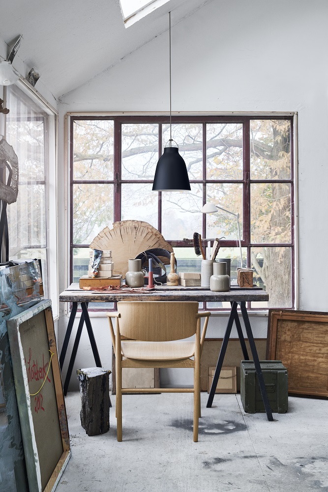 Schwarze AQ01 Pendelleuchte von Fritz Hansen über einem Schreibtisch in einem hellen Atelier mit Fenster.