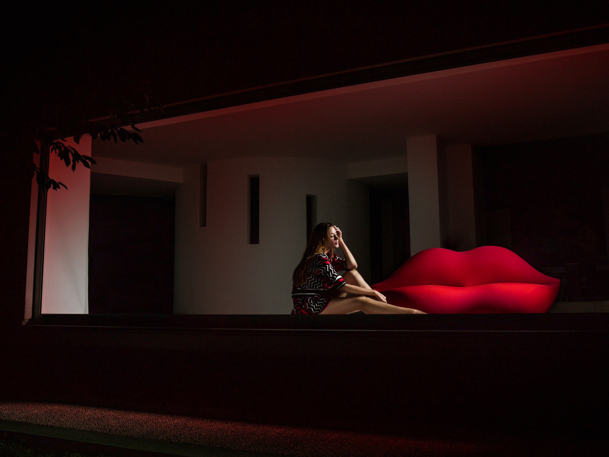 Frau sitzt auf rotem Bocca Sofa von Gufram, Lippensofa, Designmöbel für Wohnzimmer und Lounge.