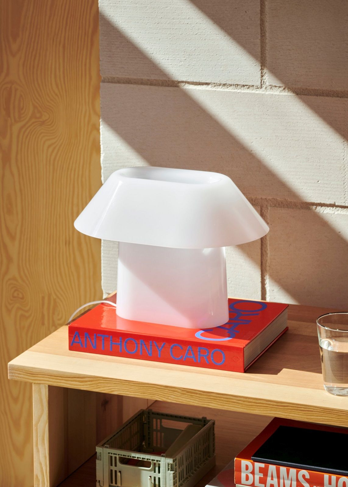 Weiße Drome Tischleuchte von Hay auf einem roten Buch, modernes Design für Wohnzimmer.