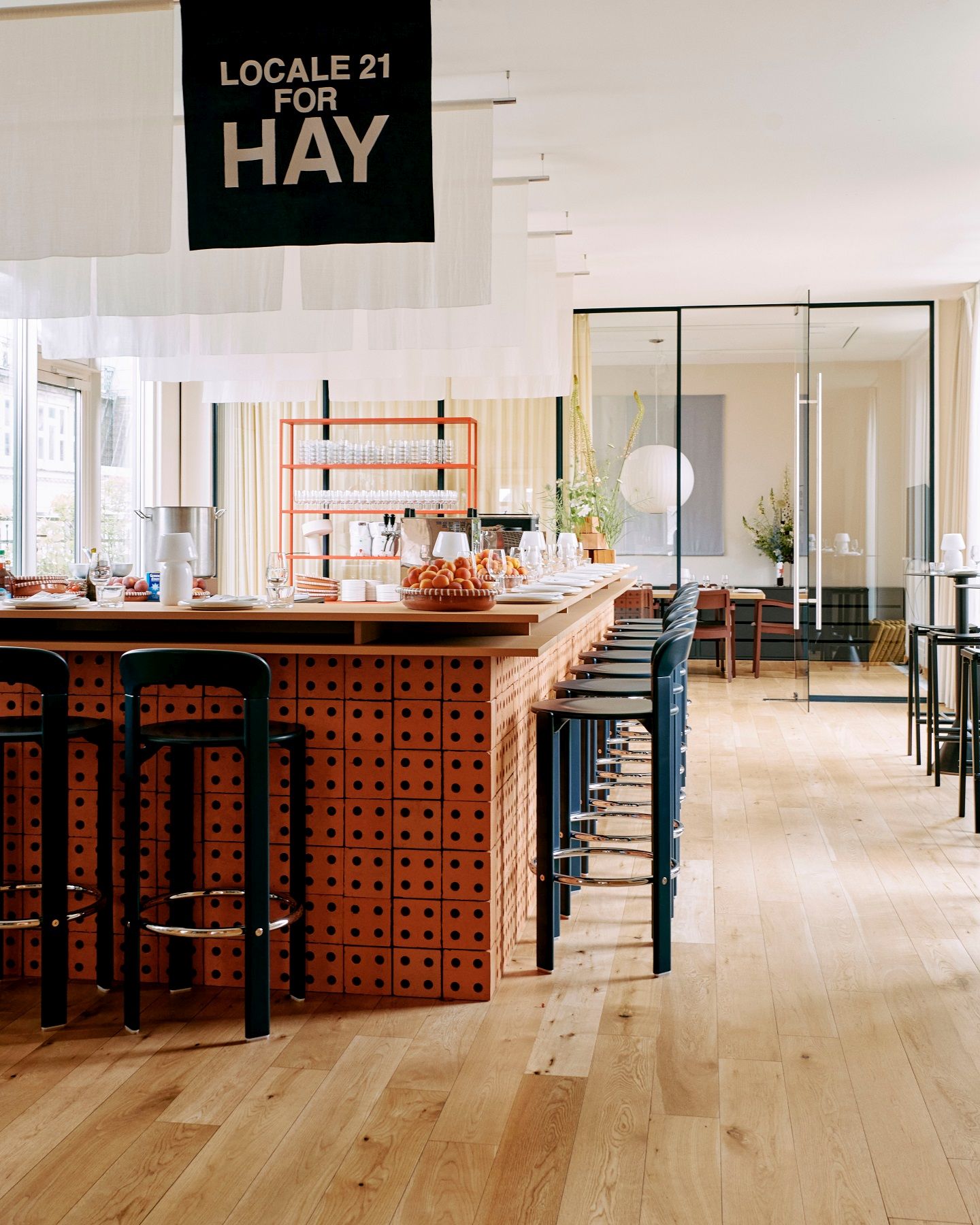 Reihe von Rey Barhockern H97cm von Hay an einer Bar mit Backsteinmuster in einem hellen Raum.