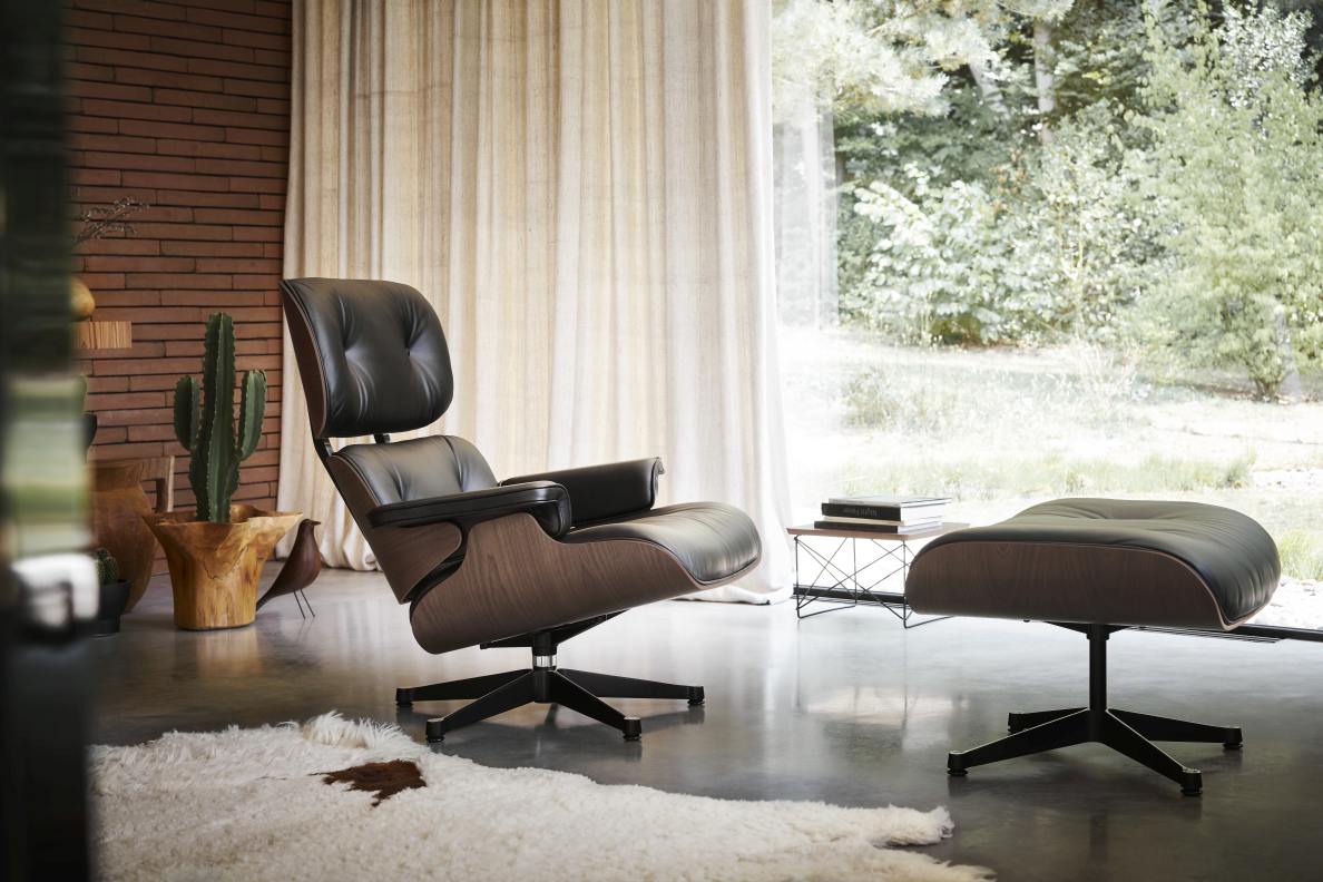 Eames Lounge Chair mit Ottoman in schwarzem Leder und dunklem Holzfurnier vor Fenster.