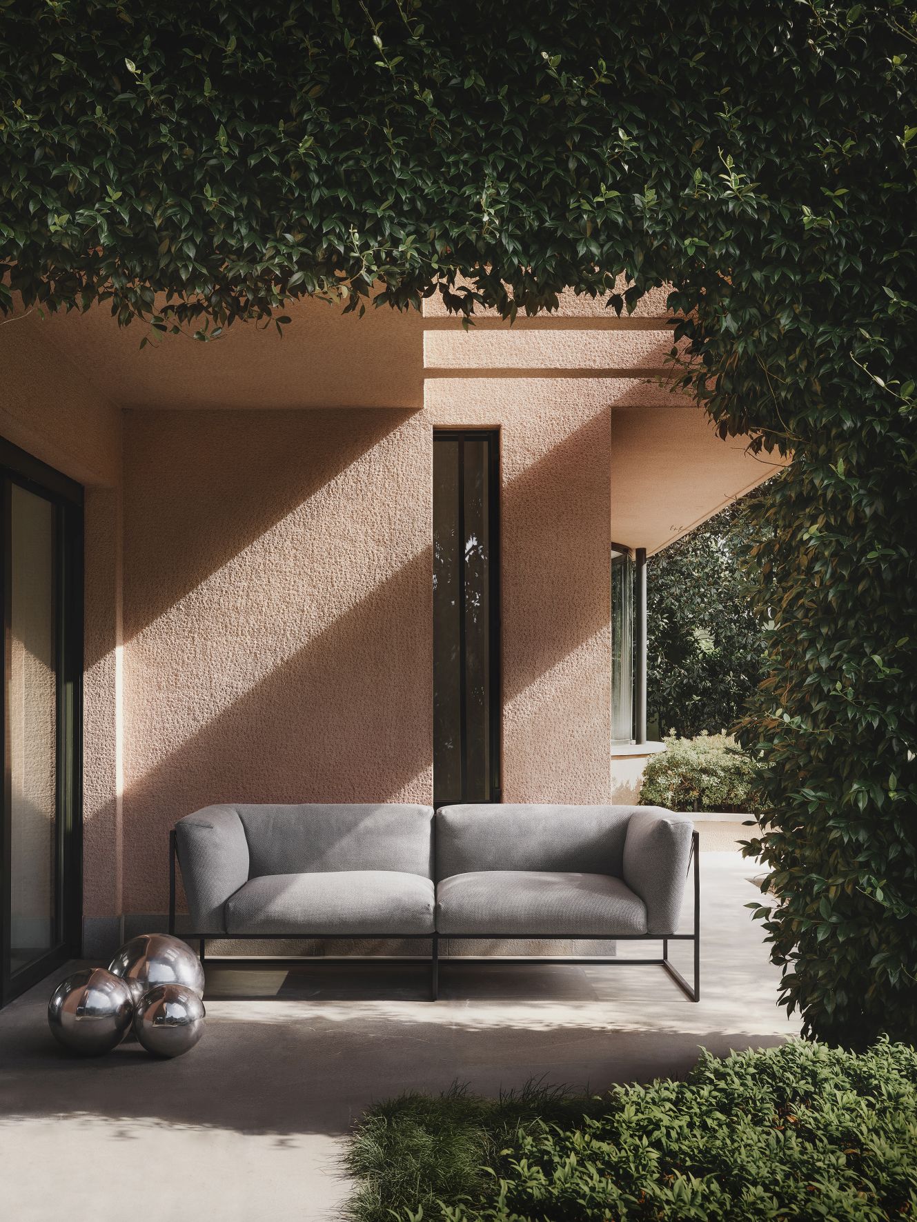 Graues Arpa Outdoor Sofa 3-Sitzer von MDF Italia auf einer Terrasse mit Pflanzen und Dekokugeln.