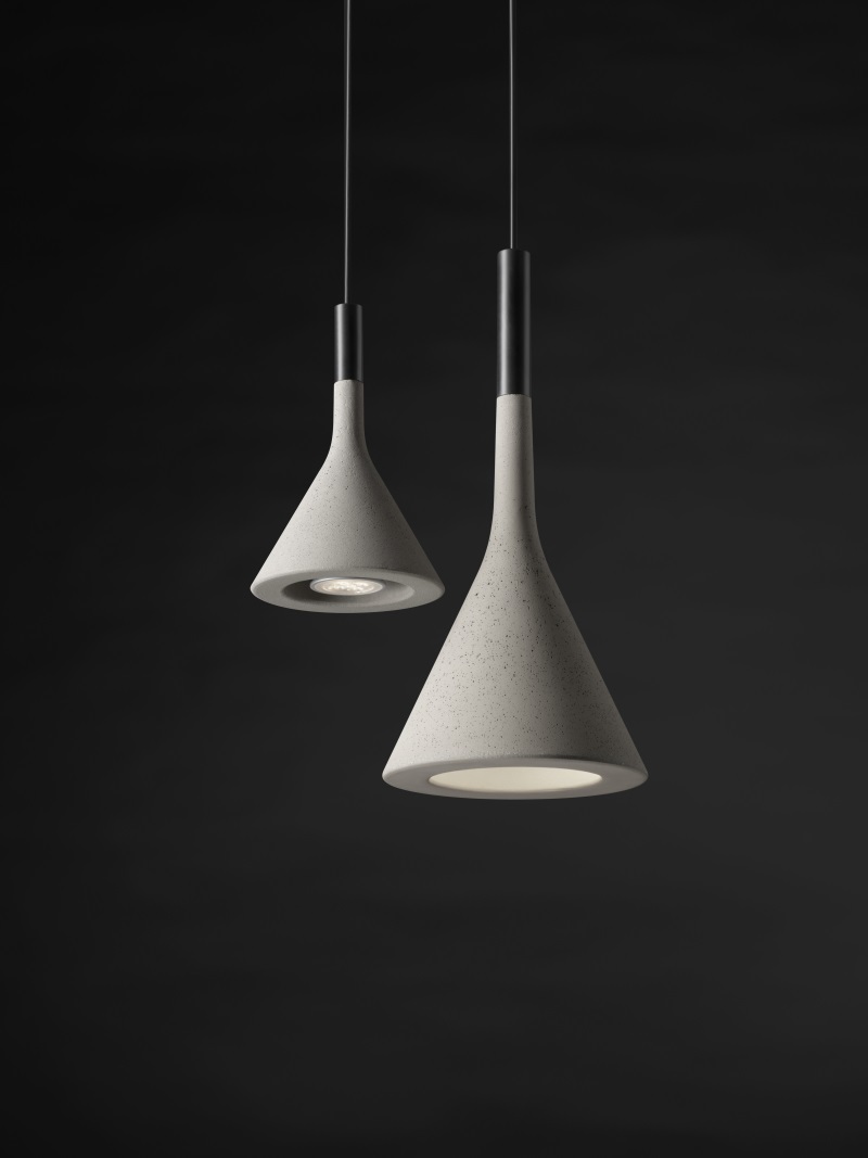 Zwei graue Aplomb Mini Pendelleuchten von Foscarini aus Beton vor dunklem Hintergrund.