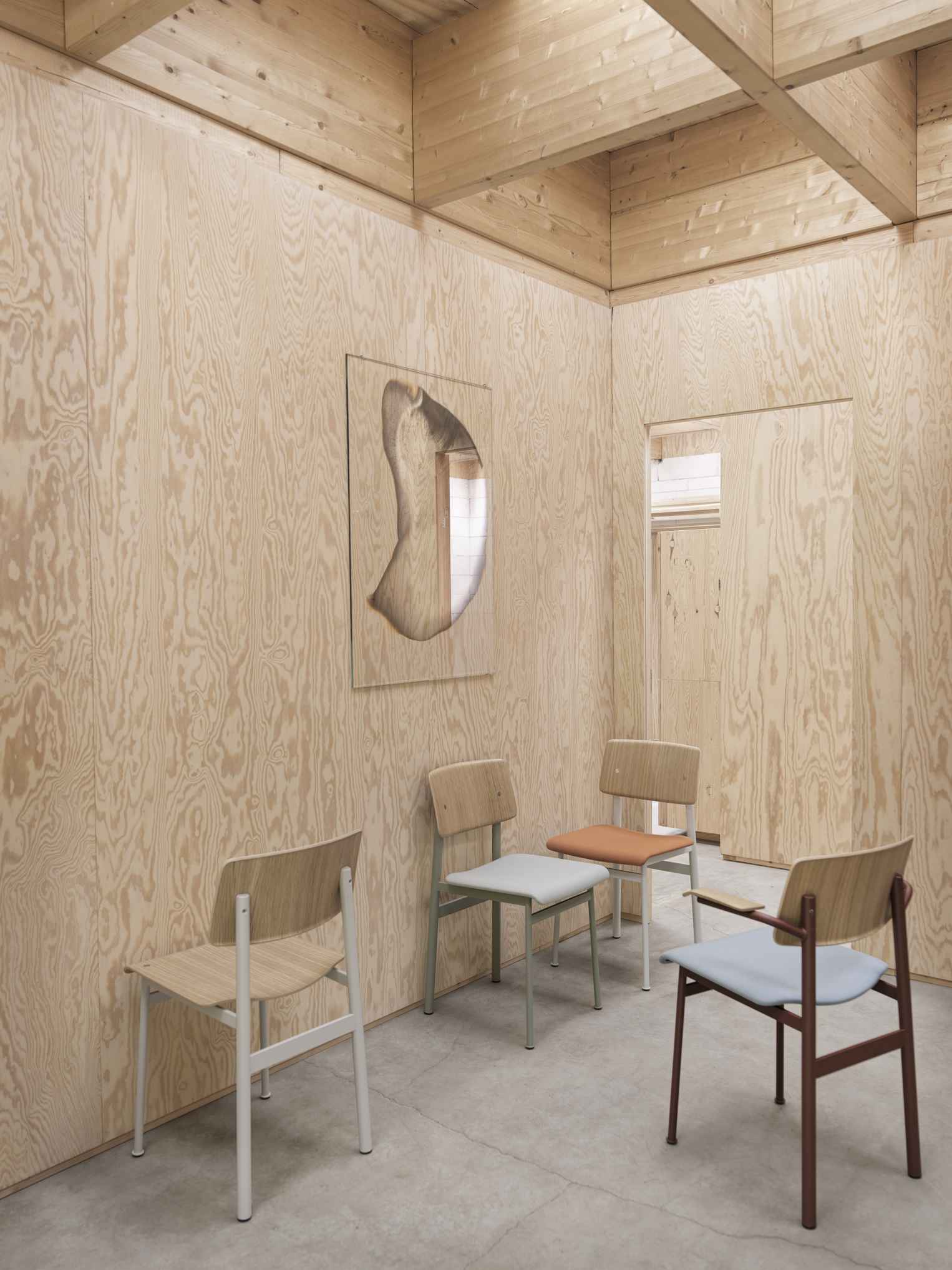Vier Muuto Loft Chair Stühle in verschiedenen Farben in einem hellen, holzvertäfelten Raum.