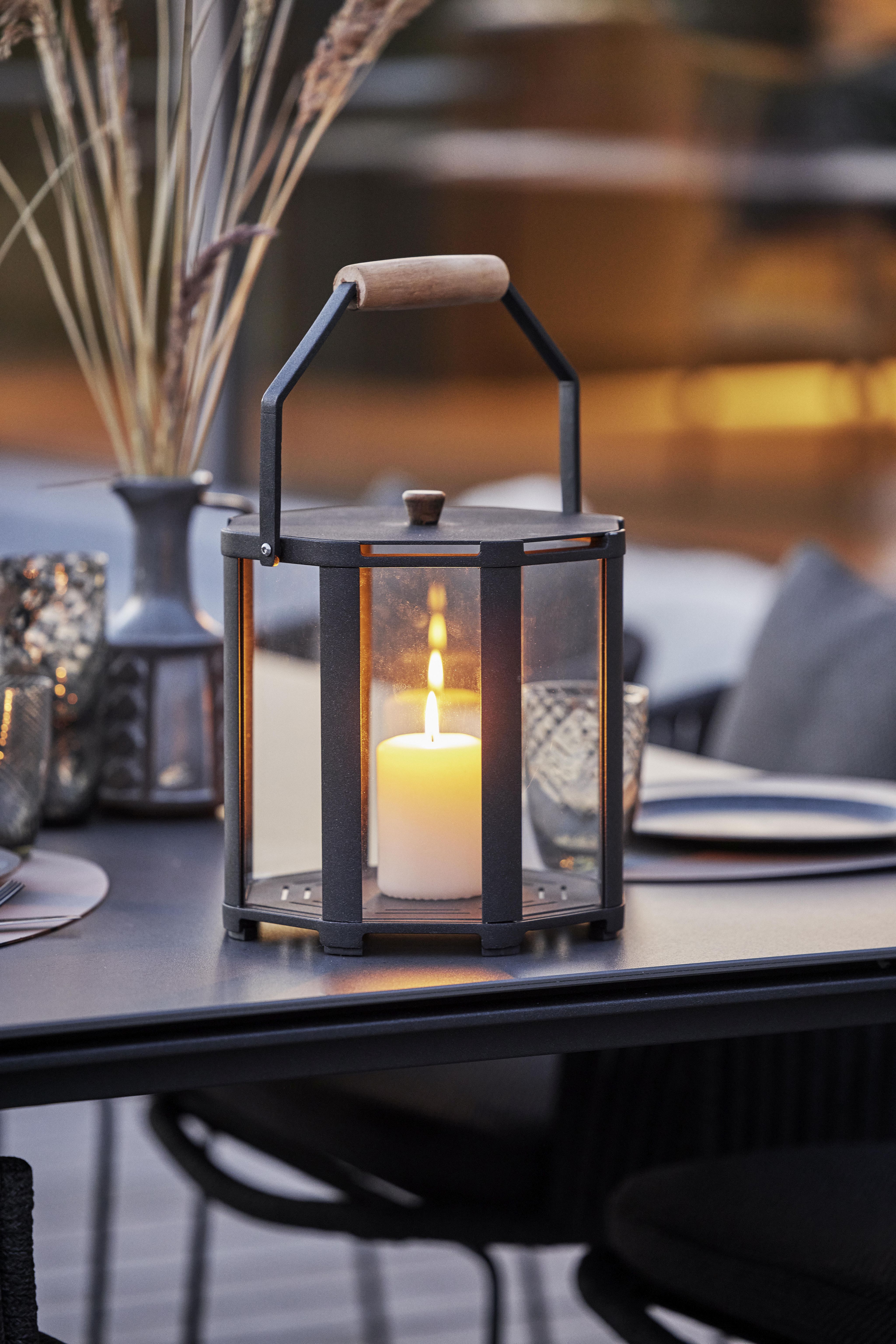 Lightlux Laterne Teak Large Cane-Line aus Teakholz und Metall mit brennender Kerze auf einem Tisch.