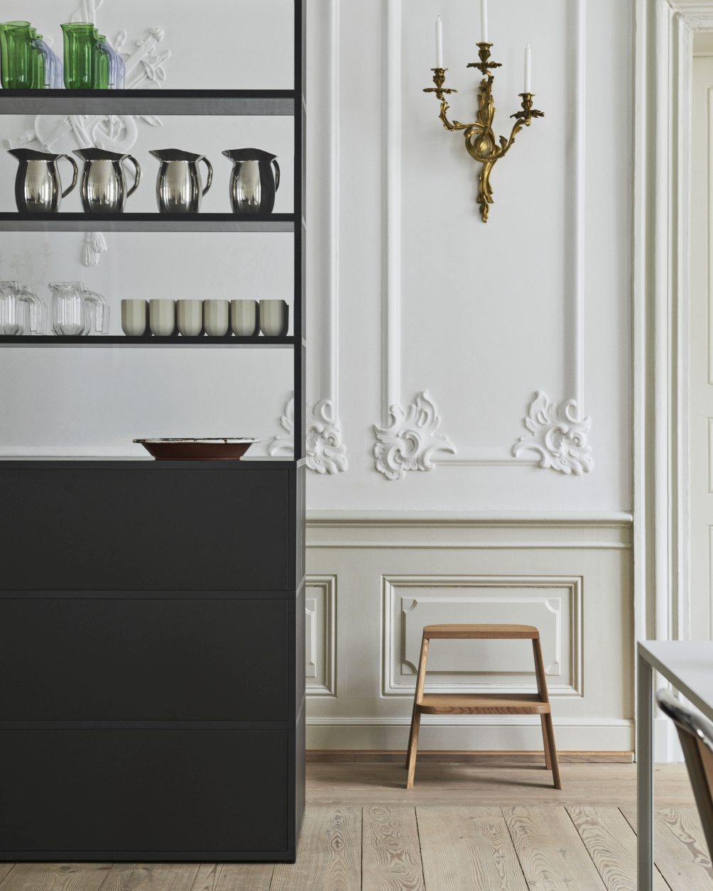 Holzhocker "Butler Hocker Hay" im Interieur mit Regalen, Geschirr und Wandleuchter auf hellem Holzboden.
