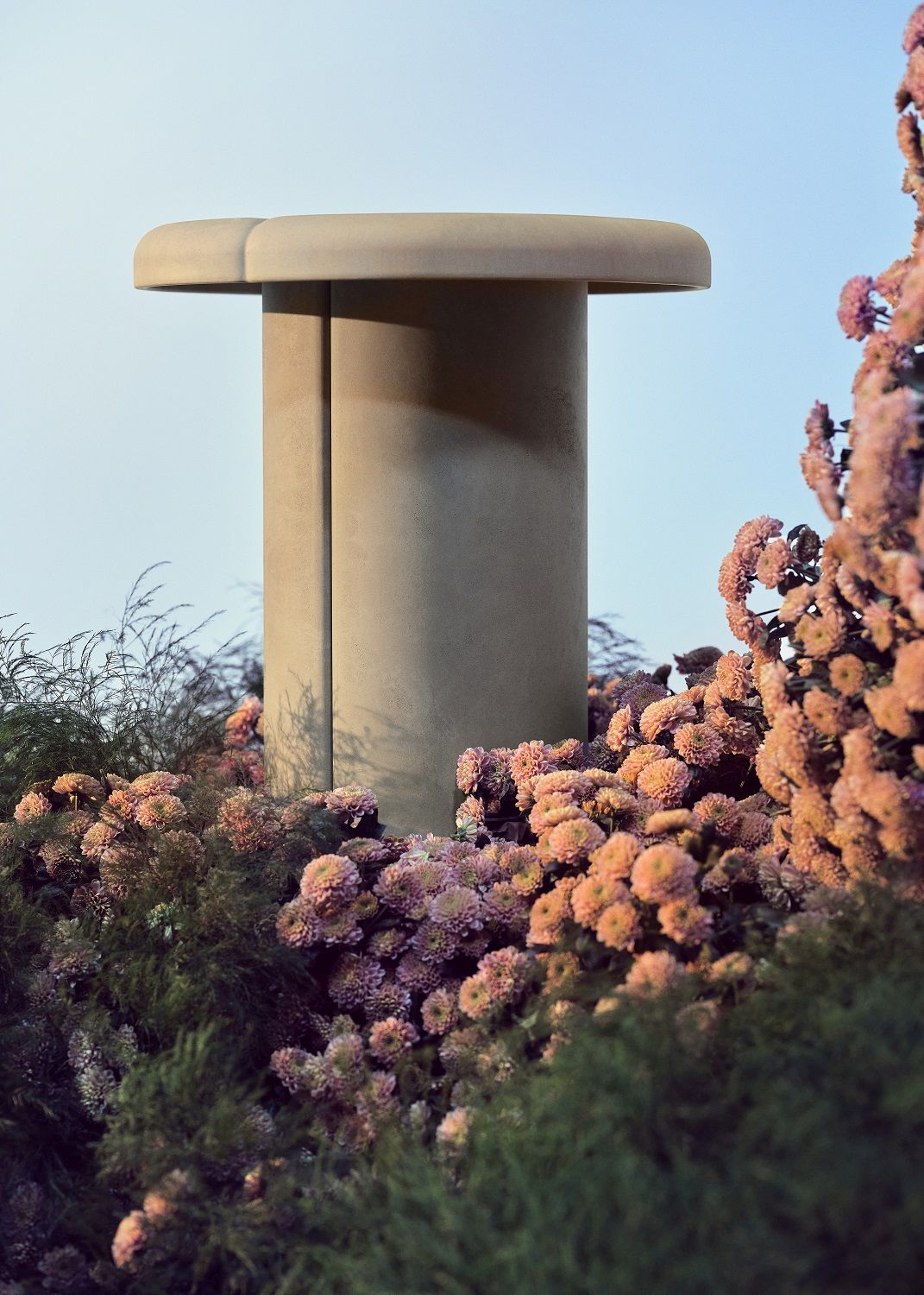 Nahaufnahme des Mater Alder Side Table Beistelltischs im Außenbereich, umgeben von rosa Blumen.