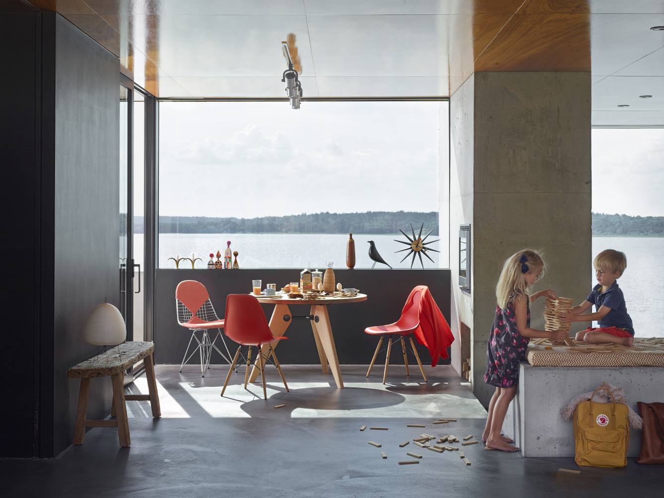 Heller Raum mit Vitra Gueridon Tisch aus Holz, roten Stühlen und spielenden Kindern am Fenster.