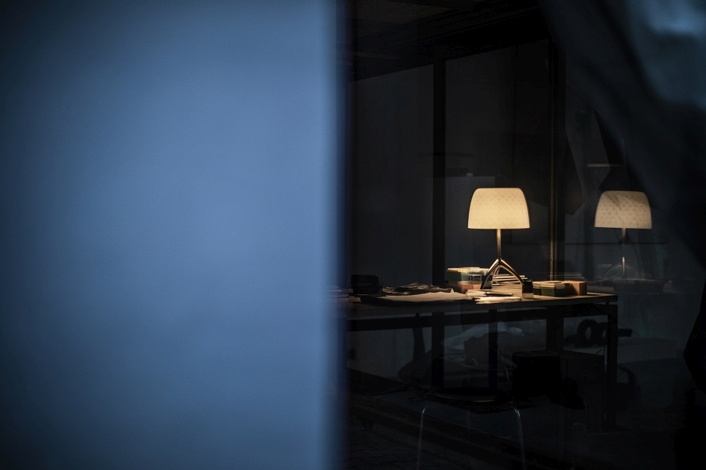 Lumiere Tischleuchte auf Schreibtisch mit Papieren und Büromaterialien, stimmungsvolle Beleuchtung im dunklen Raum.