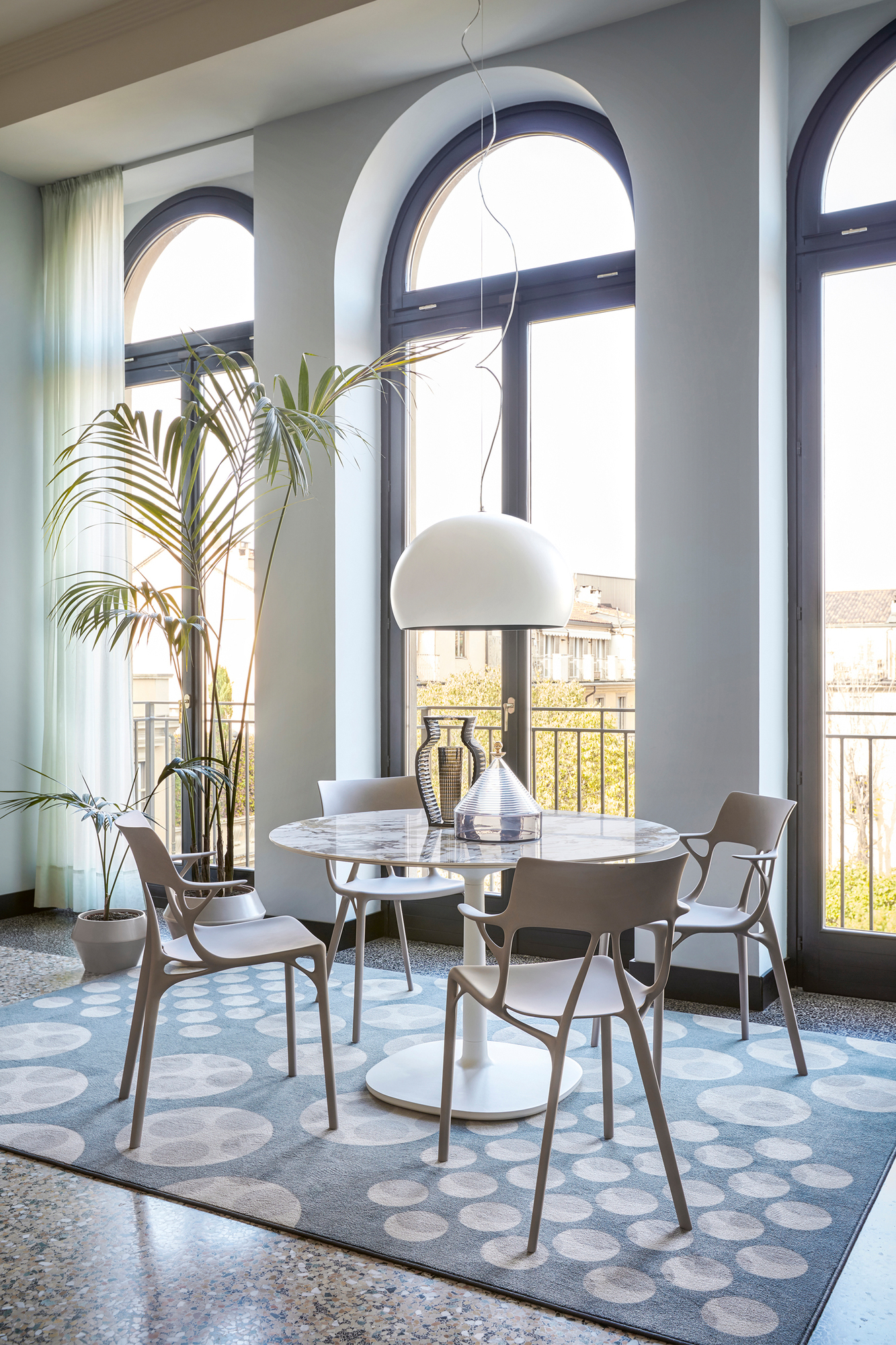 Esszimmer mit A.I. Stühlen von Kartell, modernem Design, hellen Fenstern und stilvollem Teppich.