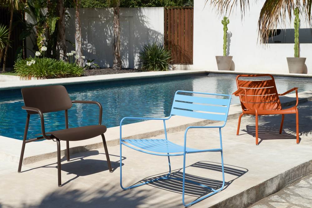 Drei farbige Fermob Studie Lounge Sessel Outdoor aus Metall stehen am Pool.