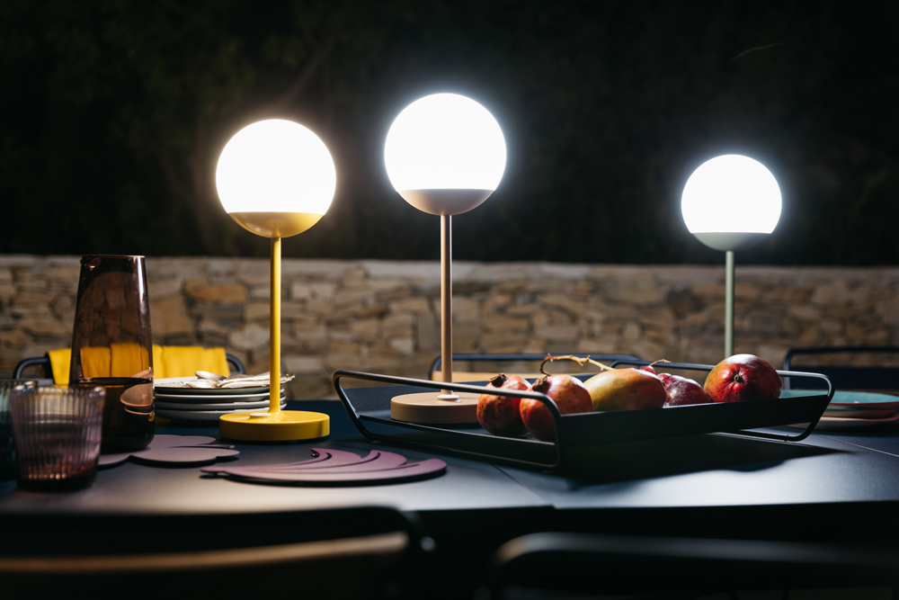 Mooon Tischleuchte von Fermob, Acapulcoblau, beleuchtet eine gedeckte Tafel im Freien. Dekorative und moderne Lampe.