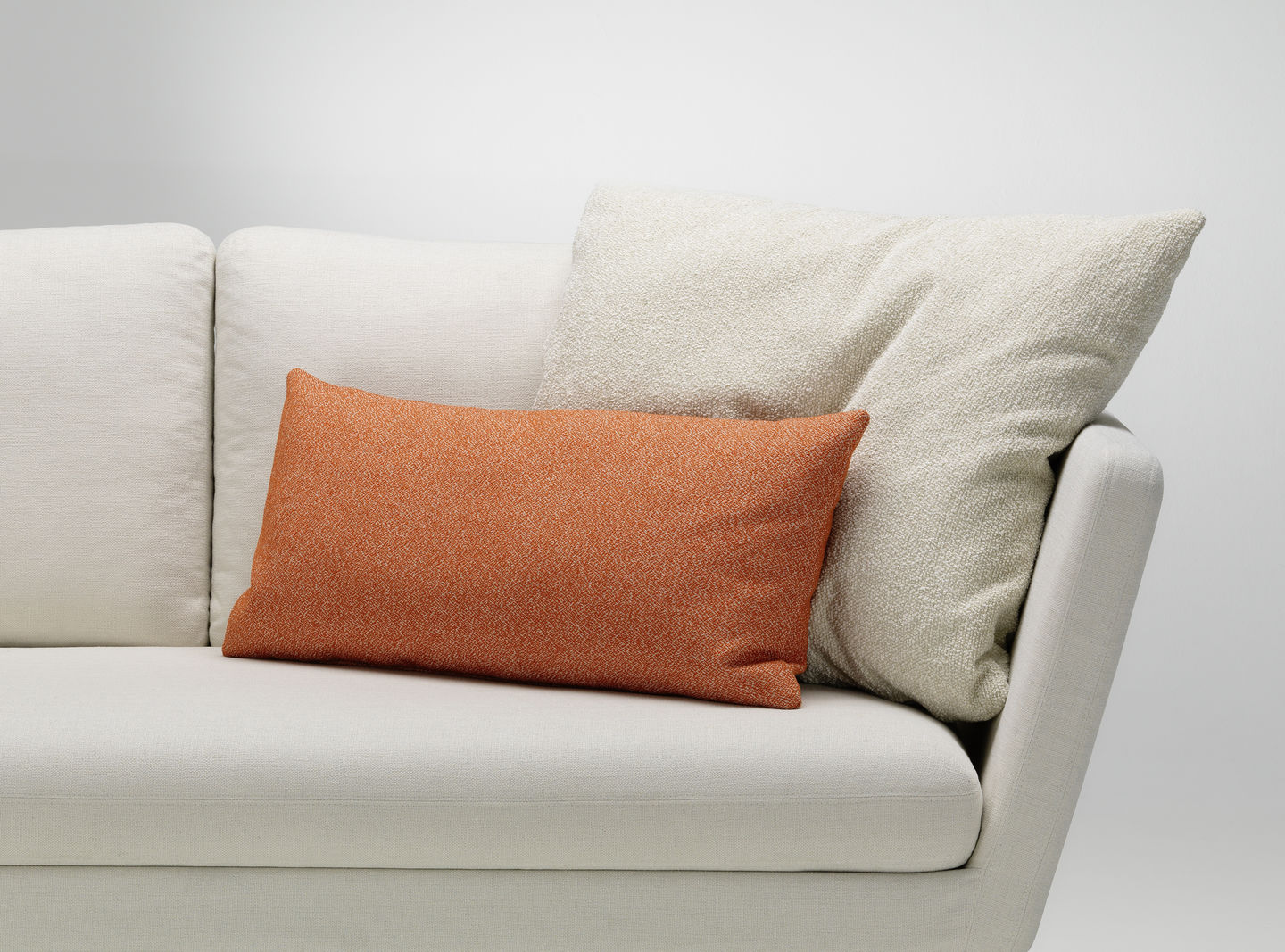 Vitra Kissen: Rechteckiges, orangefarbenes Sofakissen und quadratisches, helles Kissen auf einem cremefarbenen Sofa.