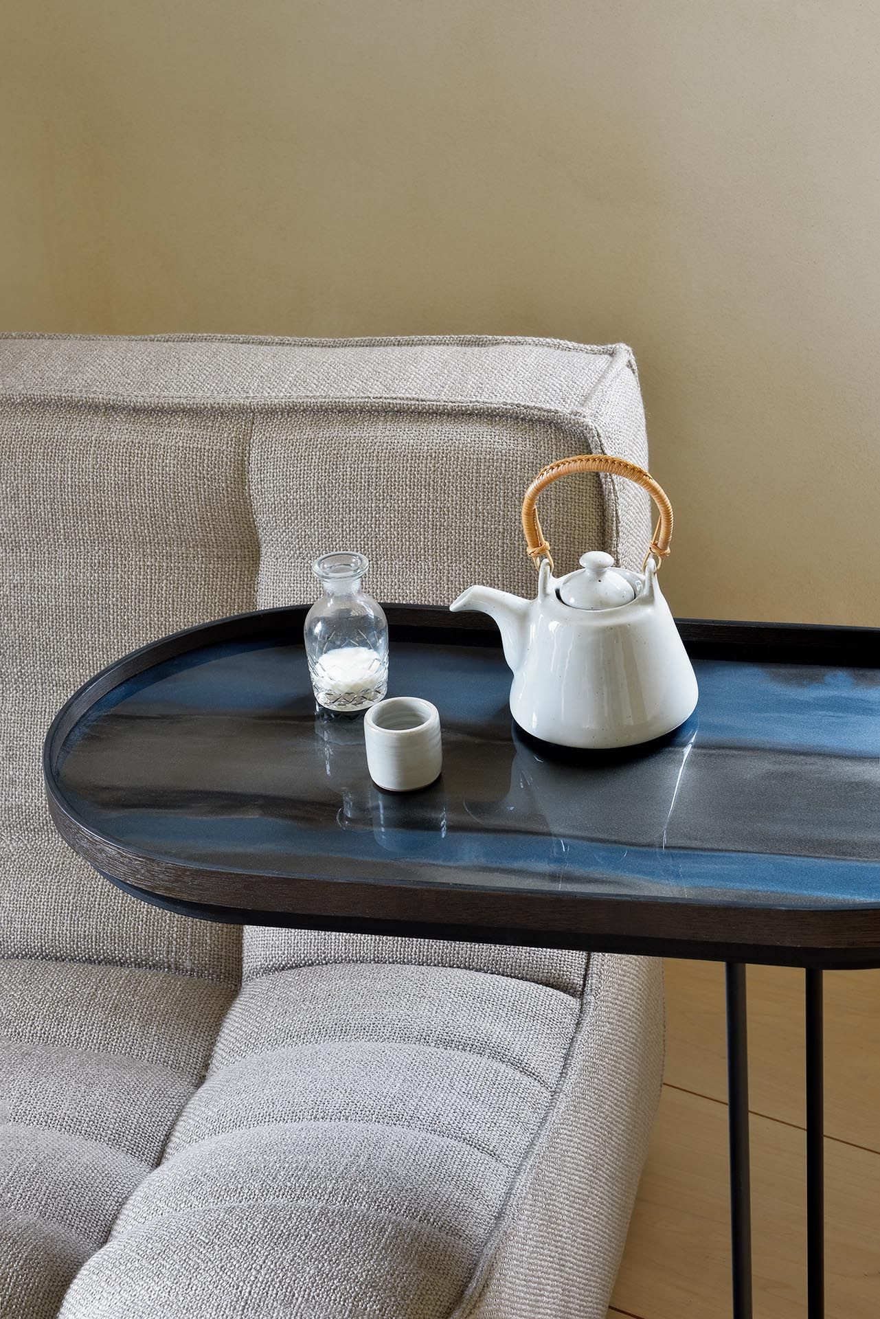 Ethnicraft Beistelltisch aus Holz, schwarz lackiert, mit Teekanne und Milchflasche neben einem Sofa.