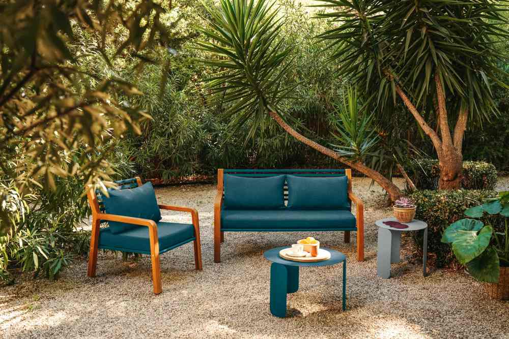 Fermob Somerset Sofa: Gartenmöbel-Set mit Zweisitzer-Sofa, Sessel und Beistelltischen in idyllischer Gartenszene.