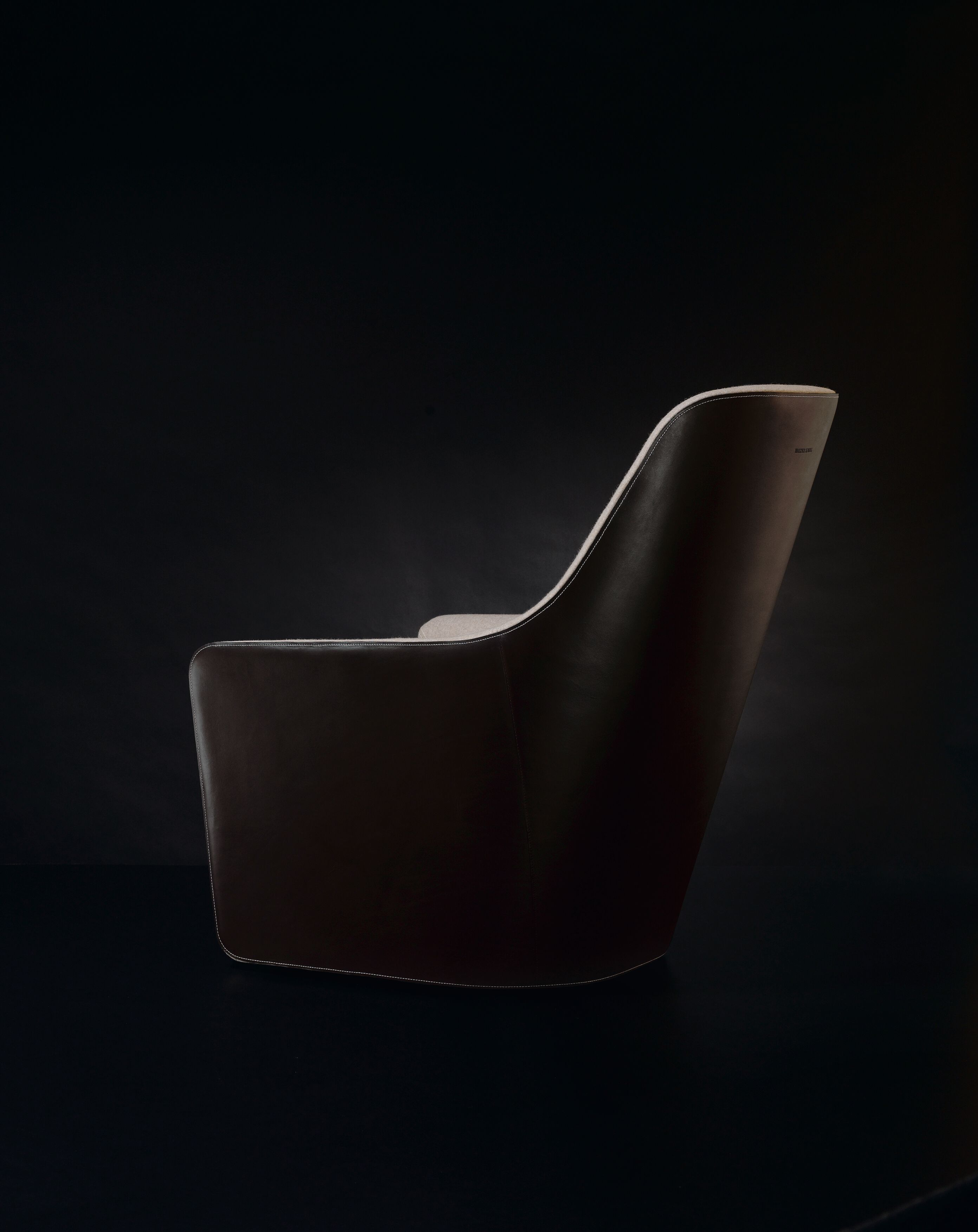 Rückansicht des braunen Walter Knoll Foster Sessels 520 mit hellgrauem Sitzpolster auf schwarzem Hintergrund.