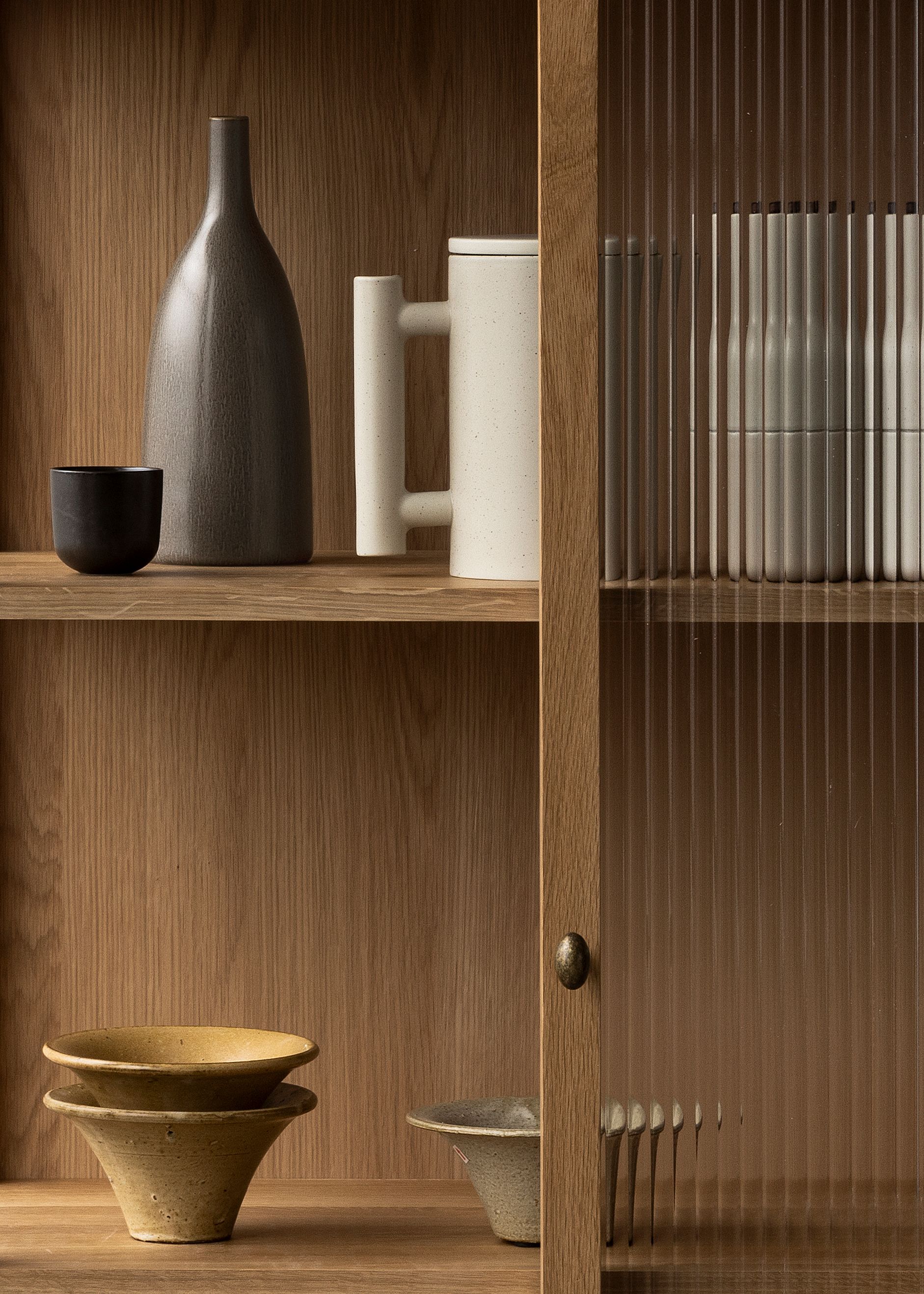 Detailaufnahme des Audo Copenhagen Curiosity Schrankes mit Glasfront und Keramikobjekten.