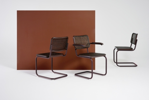Drei braune Thonet S 64 V Freischwinger Stühle mit Stahlrohr und Wiener Geflecht vor braunem Hintergrund.