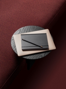 Runder, schwarzer Anagram Anstecktisch von Vitra mit Laptop, Notizbuch und Stift auf rotem Teppich.