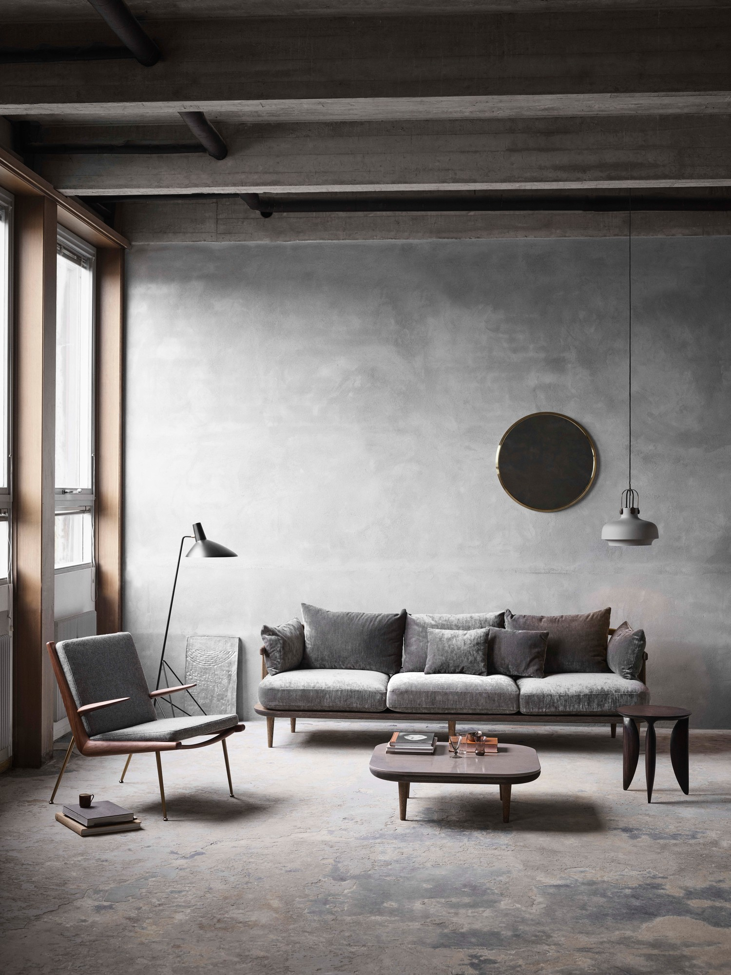 AndTradition Copenhagen SC7 Pendelleuchte über grauem Sofa in modernem Wohnzimmer mit Betonwand und Designermöbeln.