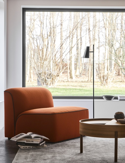 Wohnzimmer-Szene mit orangefarbenem Sessel und grauem Woud Tint Rug Teppich 170x240 cm vor großem Fenster.