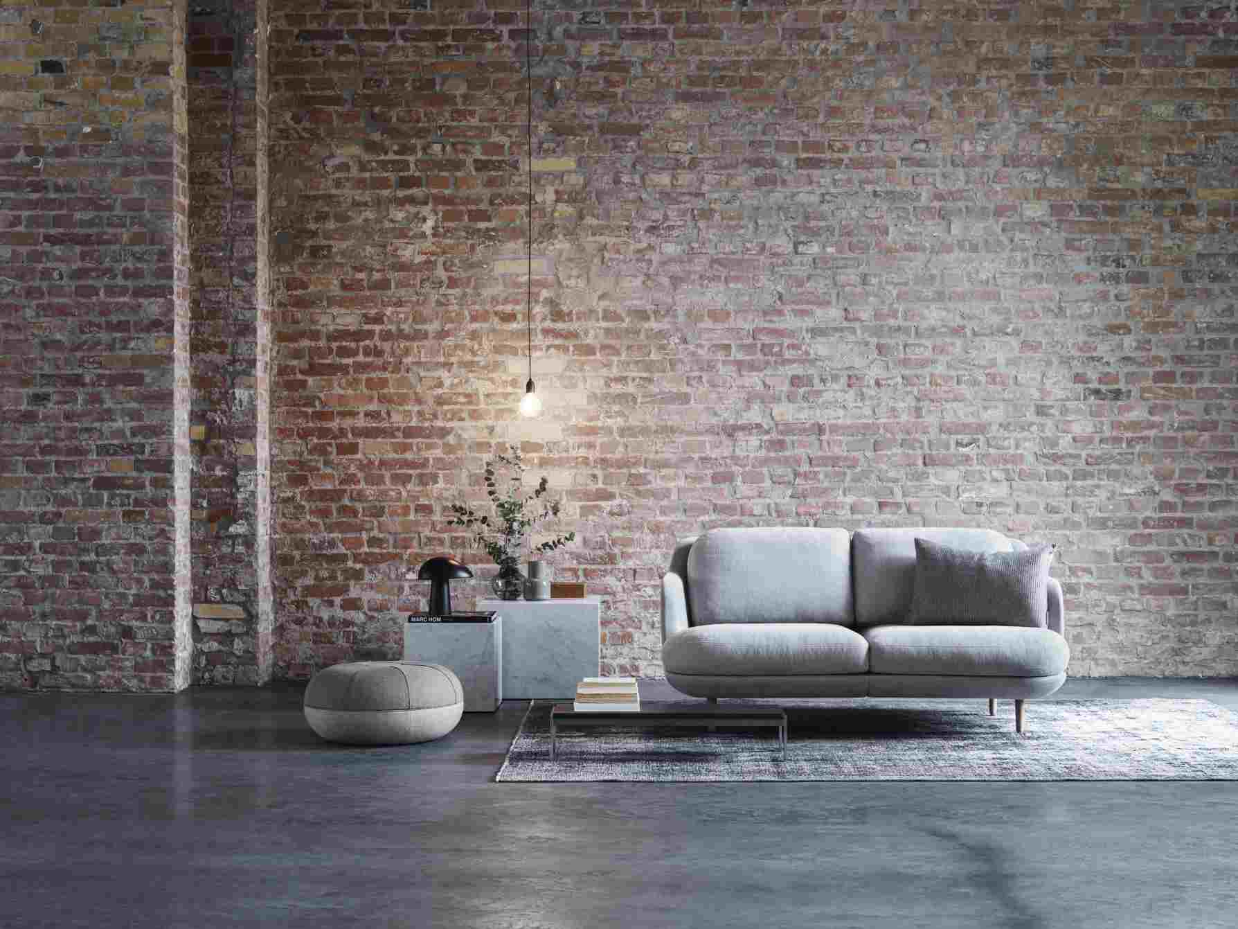 Graues Fritz Hansen Lune Sofa 2-Sitzer vor einer Backsteinwand, mit Beistelltisch und Teppich.