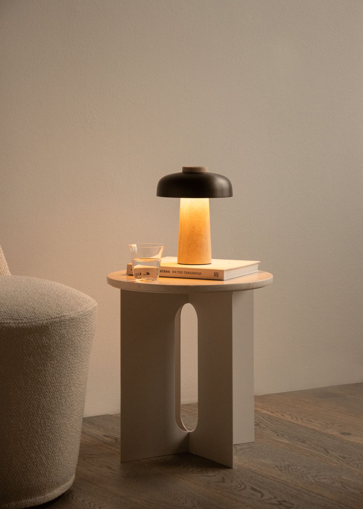 Audo Copenhagen Reverse Akkuleuchte auf Nachttisch mit Buch und Wasserglas, warmes Licht.