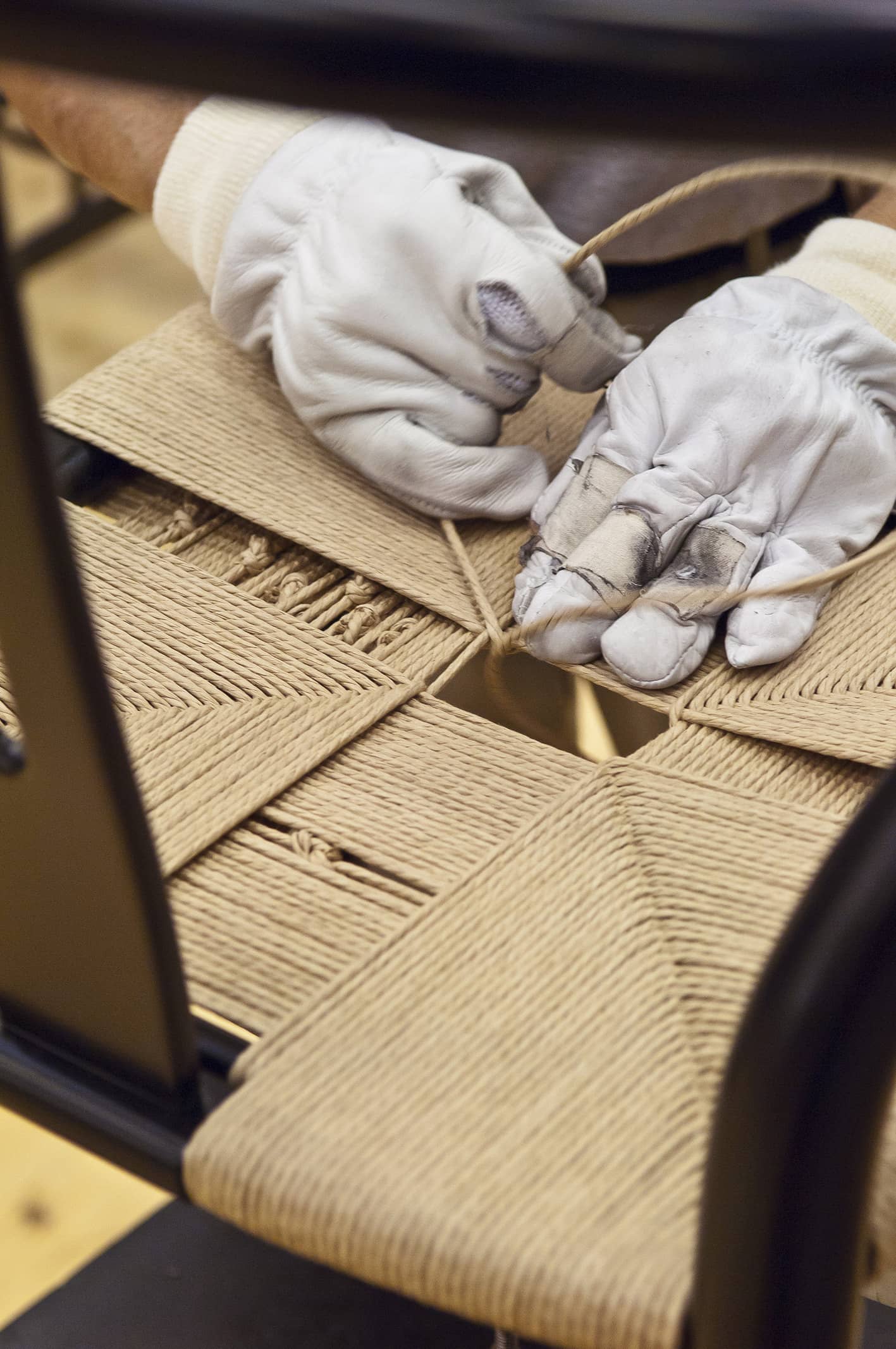 Handwerker flechtet mit Handschuhen einen Stuhl mit Seilgeflecht, traditionelle Handwerkskunst für Möbel.