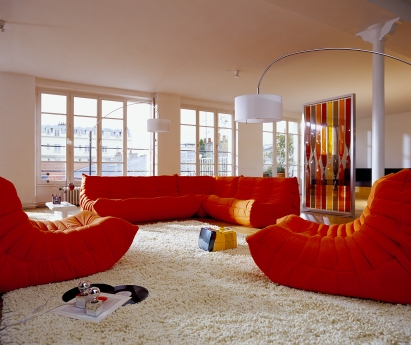 Oranges Togo Eckteil Sofa von ligne roset in modernem Wohnzimmer mit Teppich und Fenstern.