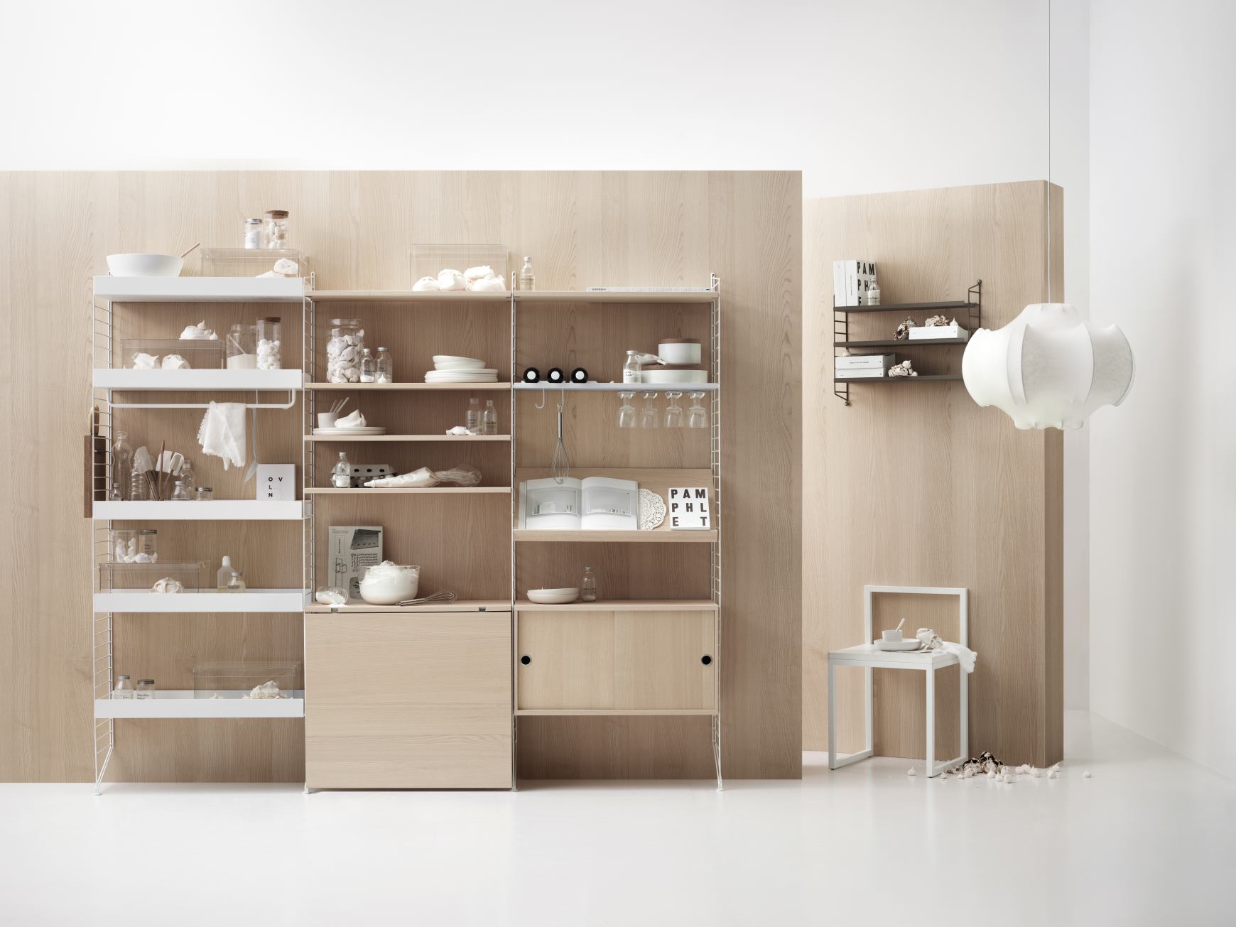 Wohnzimmer mit String Furniture Regalsystem in Weiß und Holz, minimalistisch dekoriert mit Geschirr und Gläsern.