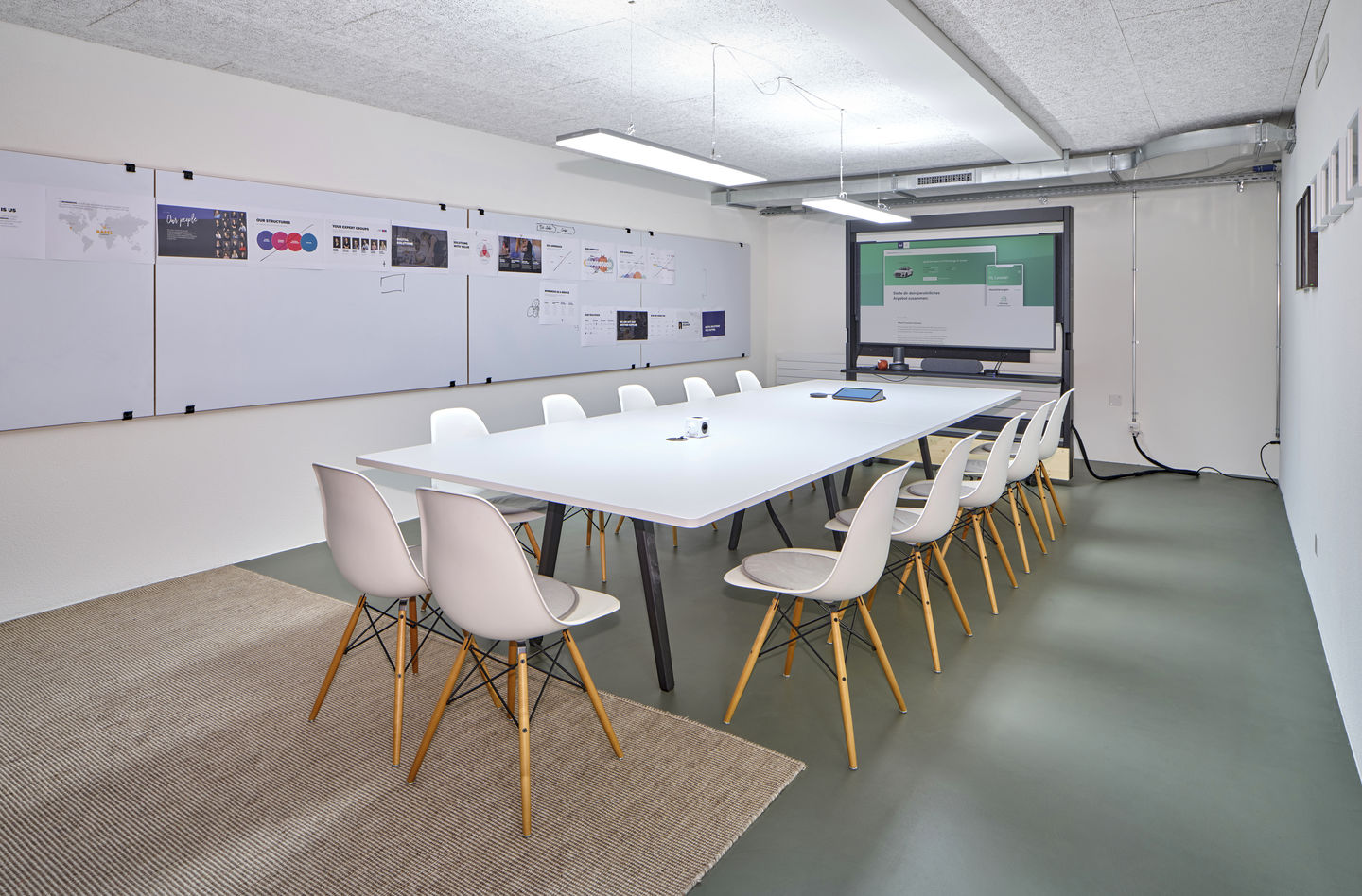 Konferenzraum mit langem Tisch und mehreren weißen Eames DSW Stühlen mit Sitzpolster von Vitra.