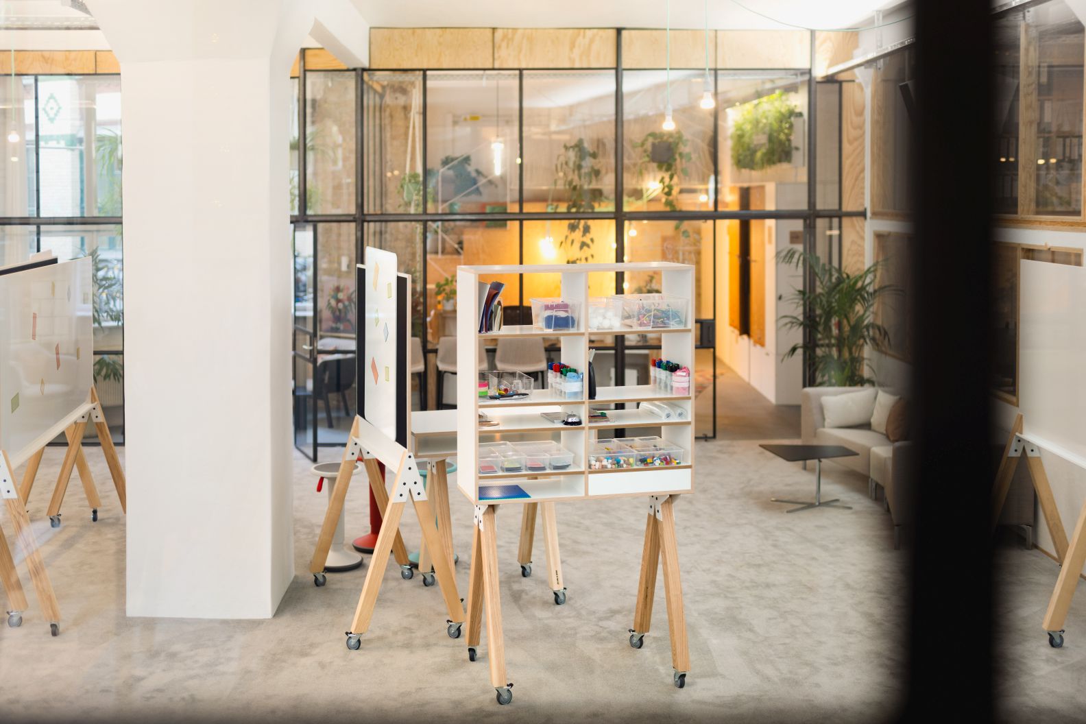 What if We Fly Taskboard: Helles Büro mit mobiler Medienwand, Whiteboards und Stauraumelementen.