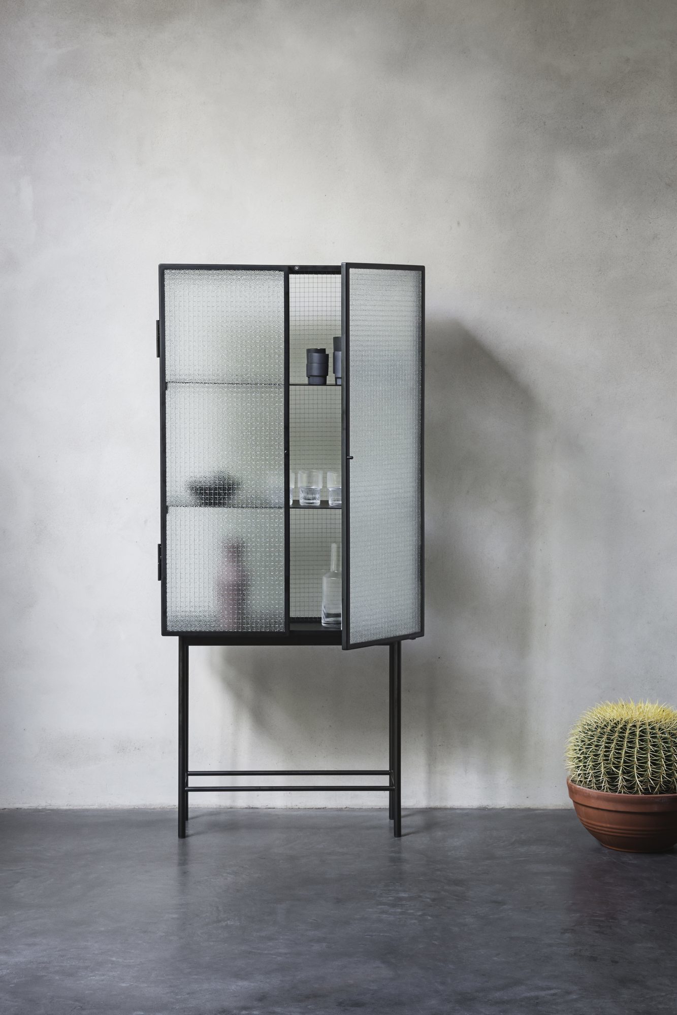 Ferm Living Haze Vitrine mit zwei Glas-Schiebetüren, schwarzem Metallrahmen und minimalistischem Design im Wohnzimmer.