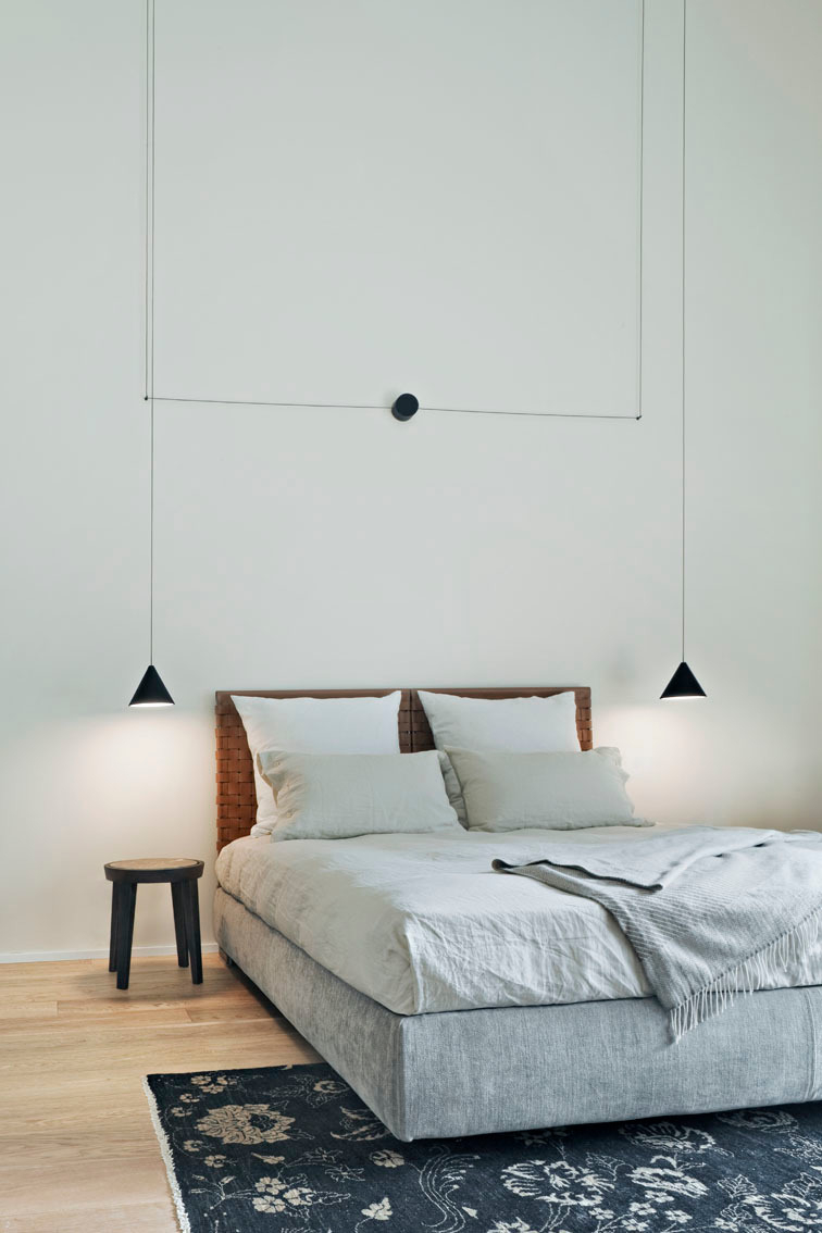 Schlafzimmer mit Flos String Light Cone Pendelleuchten als Nachttischlampen, minimalistisches Design und indirektes Licht.