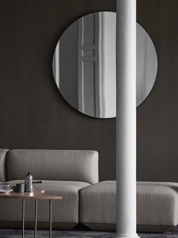 AndTradition Pinwheel HM7 Beistelltisch neben Sofa mit Kaffeekanne und rundem Spiegel an dunkler Wand.