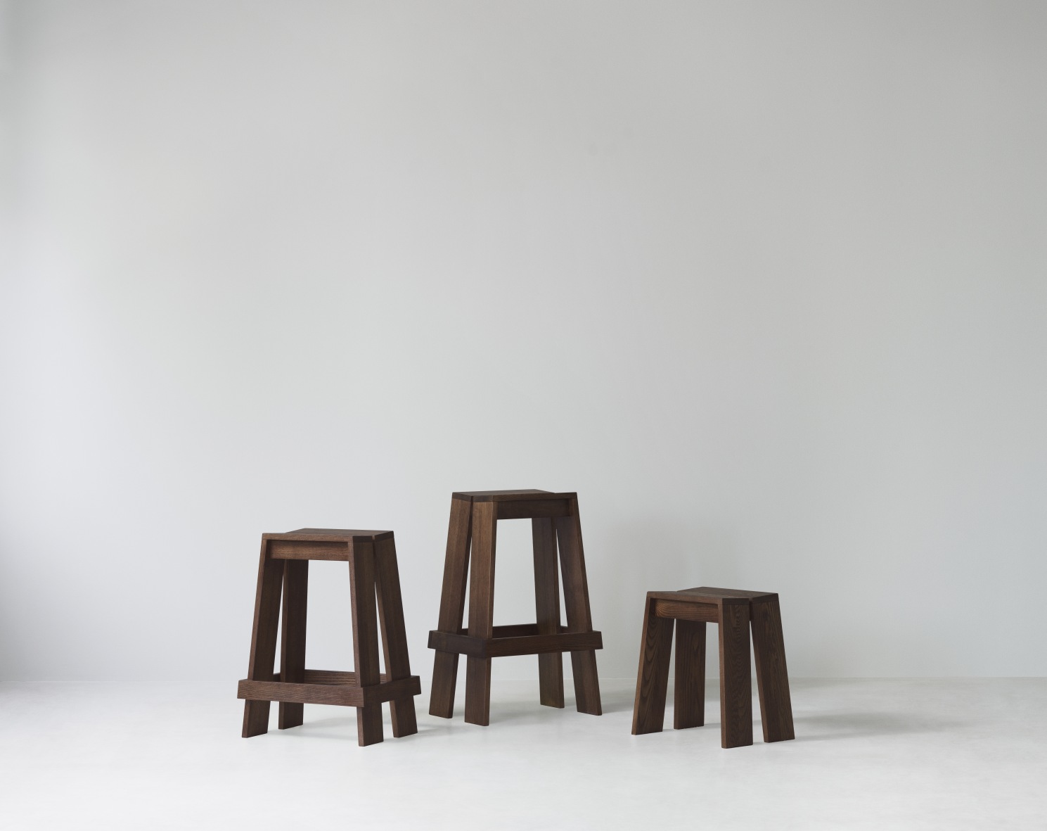 Drei braune Let Barhocker von Normann Copenhagen in verschiedenen Höhen vor einer weißen Wand.