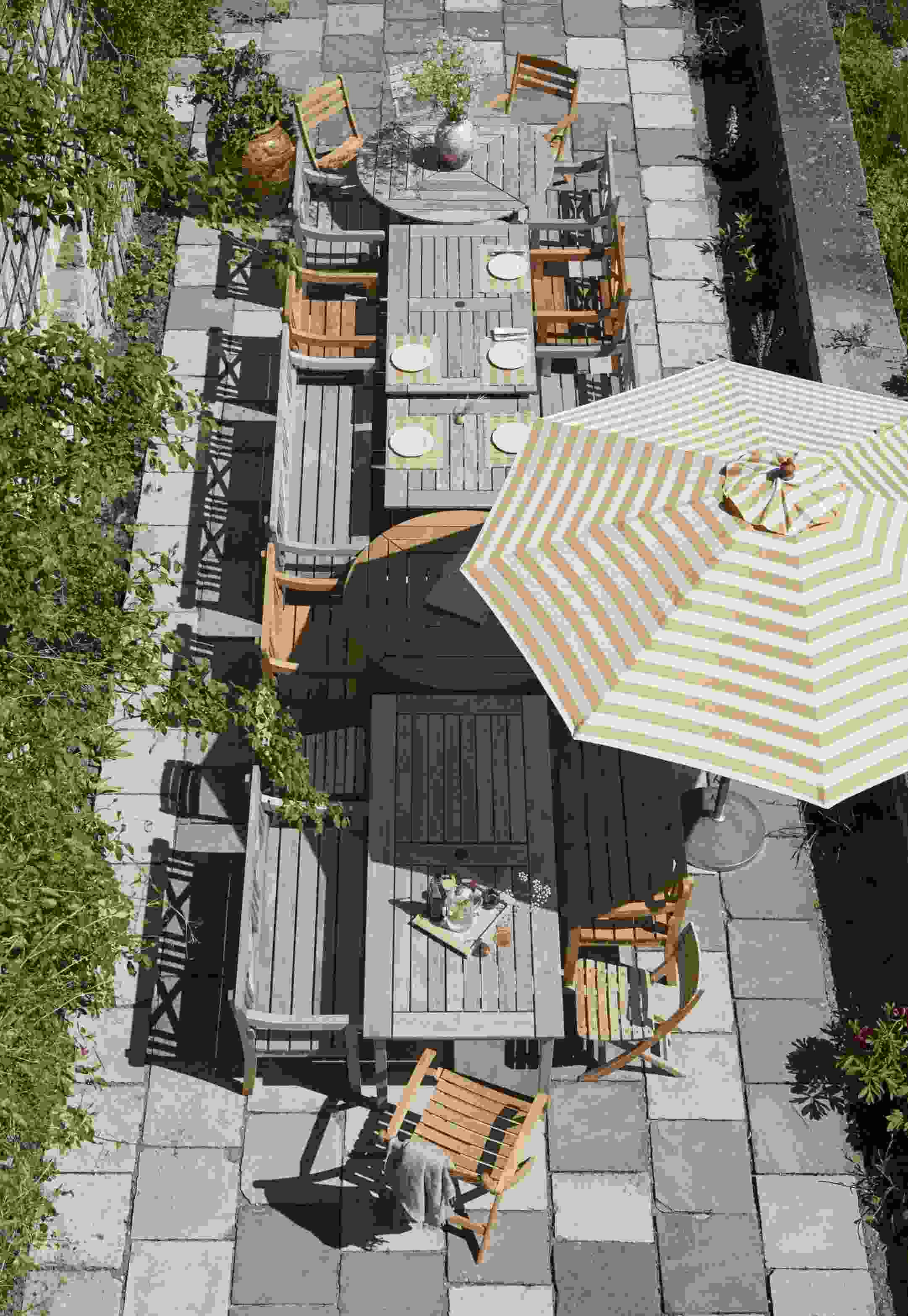 Draufsicht auf eine Gartenterrasse mit mehreren Holztischen und Drachmann Stühlen von Skagerak by Fritz Hansen.