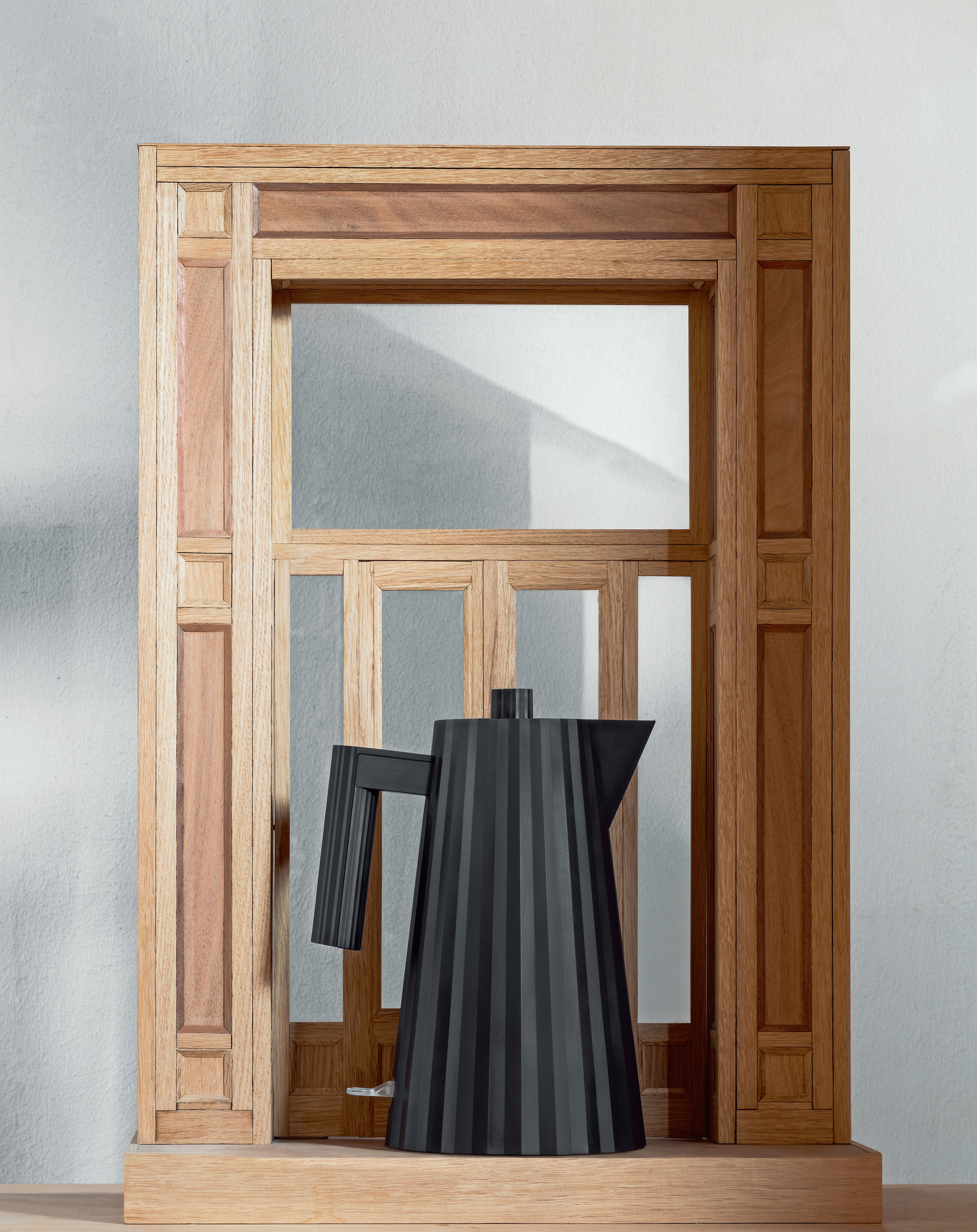 Grauer Alessi MDL06 Plissé Wasserkocher vor Holzrahmen, modernes Küchendesign.
