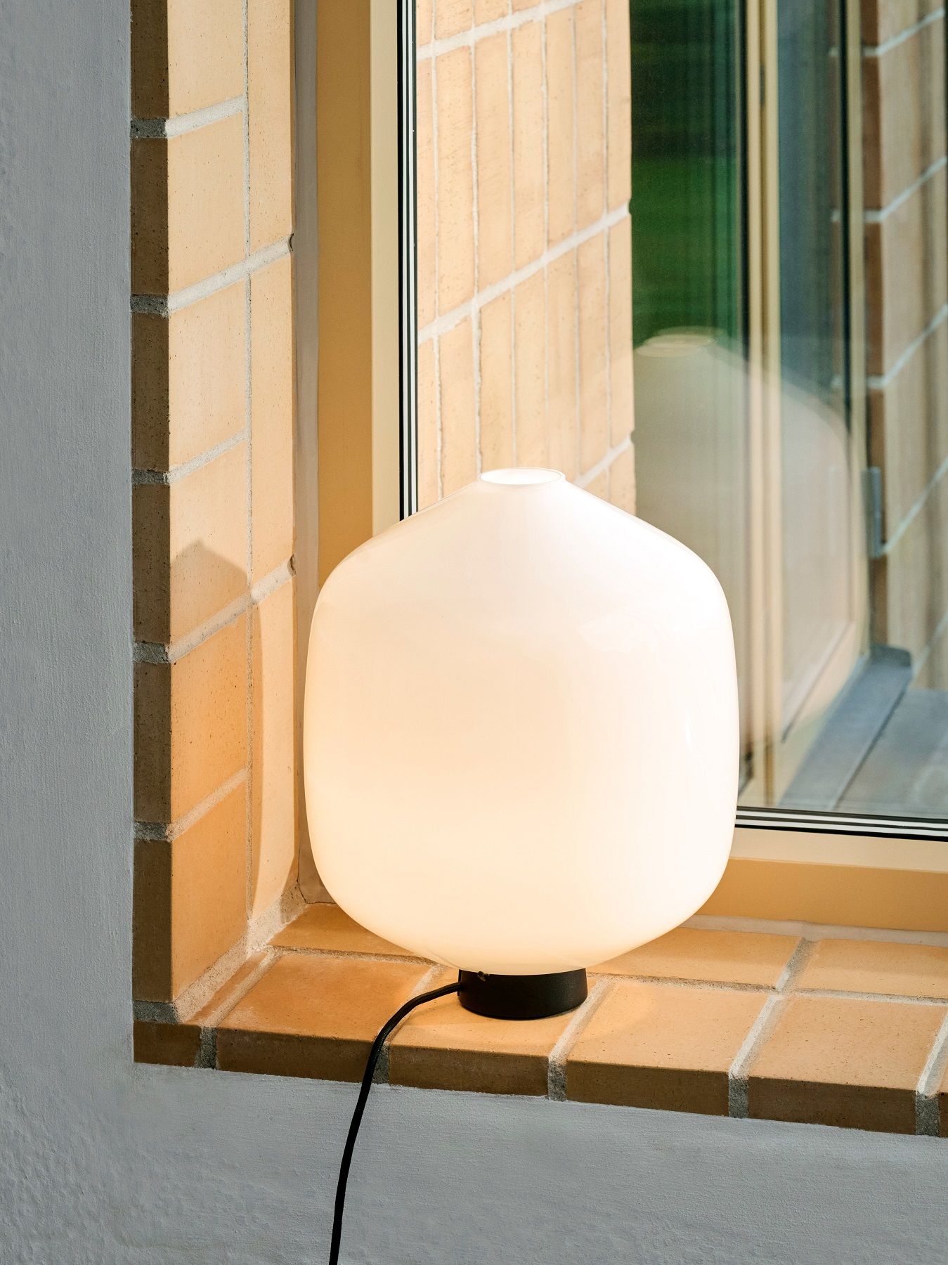 Nahaufnahme der Aspekt Buoy Tischleuchte von Hay, mit sanftem Lichtschein auf einer Fensterbank.