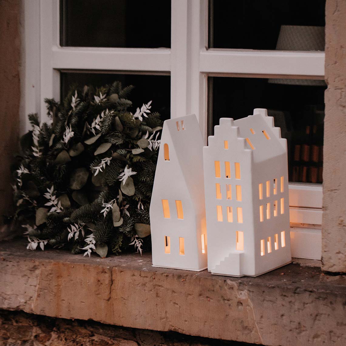 Zwei weiße Lichthäuser mit Giebeldach als stimmungsvolle Weihnachtsdeko auf einer Fensterbank.