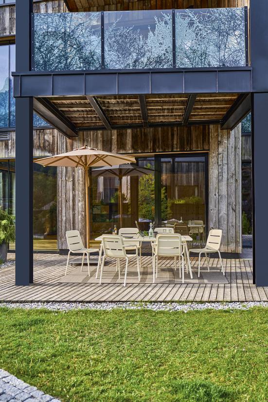 Weishäupl Vapio Stuhl Outdoor: Gartensitzgruppe mit beigen Stühlen und Tisch unter Sonnenschirm auf Holzterrasse.