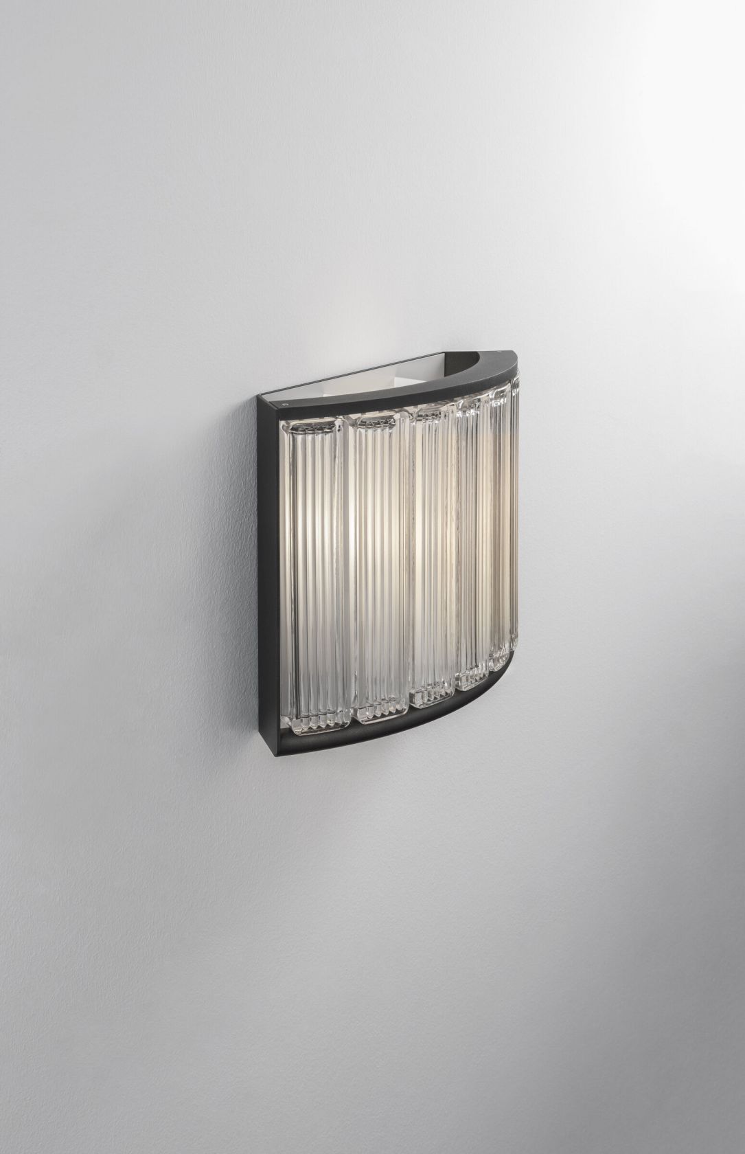Estadio Wandleuchte von Santa & Cole: Halbmondförmige Wandlampe mit geriffelten Glasstäben und schwarzem Rahmen.