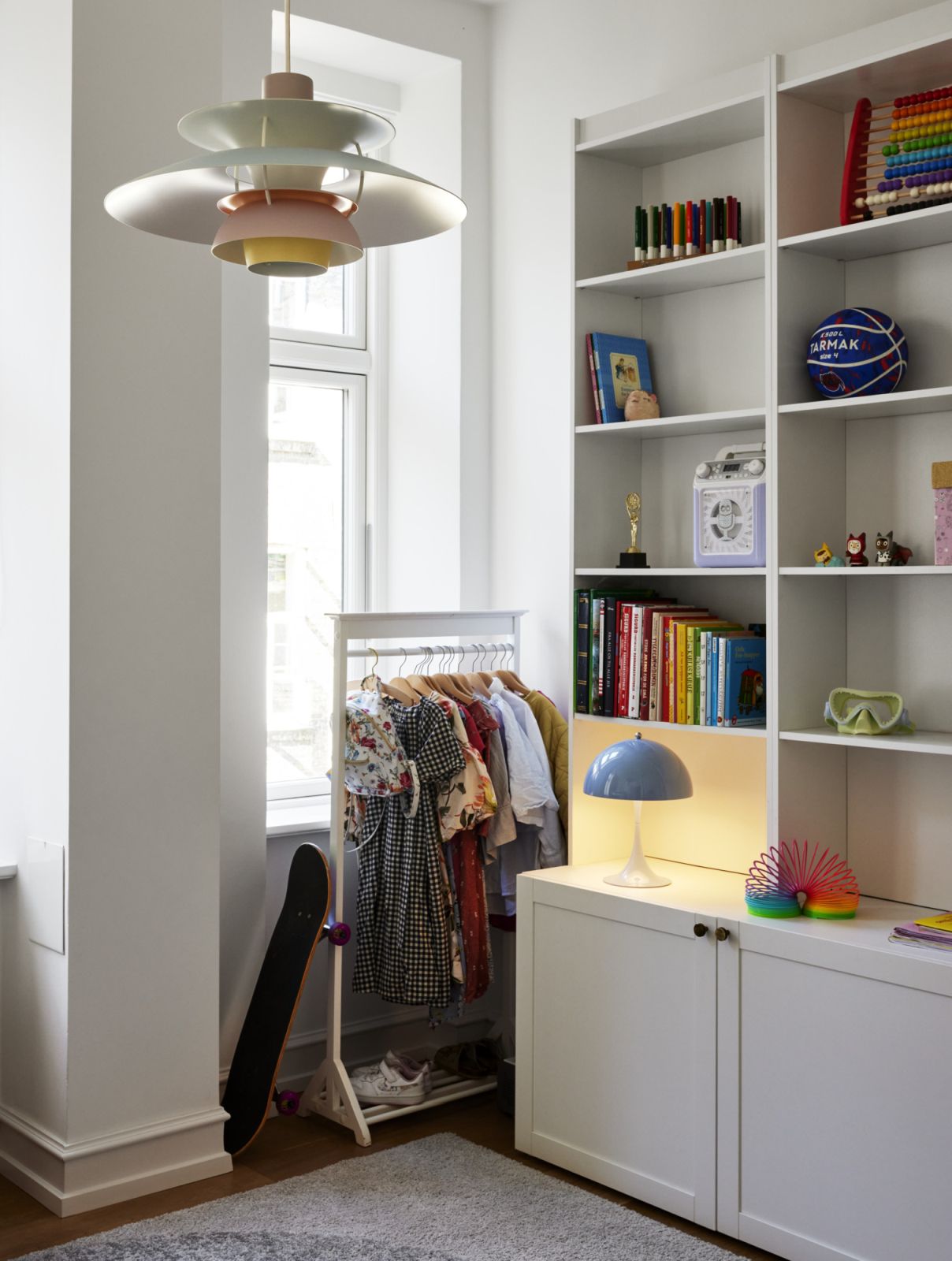 Kinderzimmer mit Kleiderständer, Skateboard, Bücherregal und Spielzeug für Jungen und Mädchen.